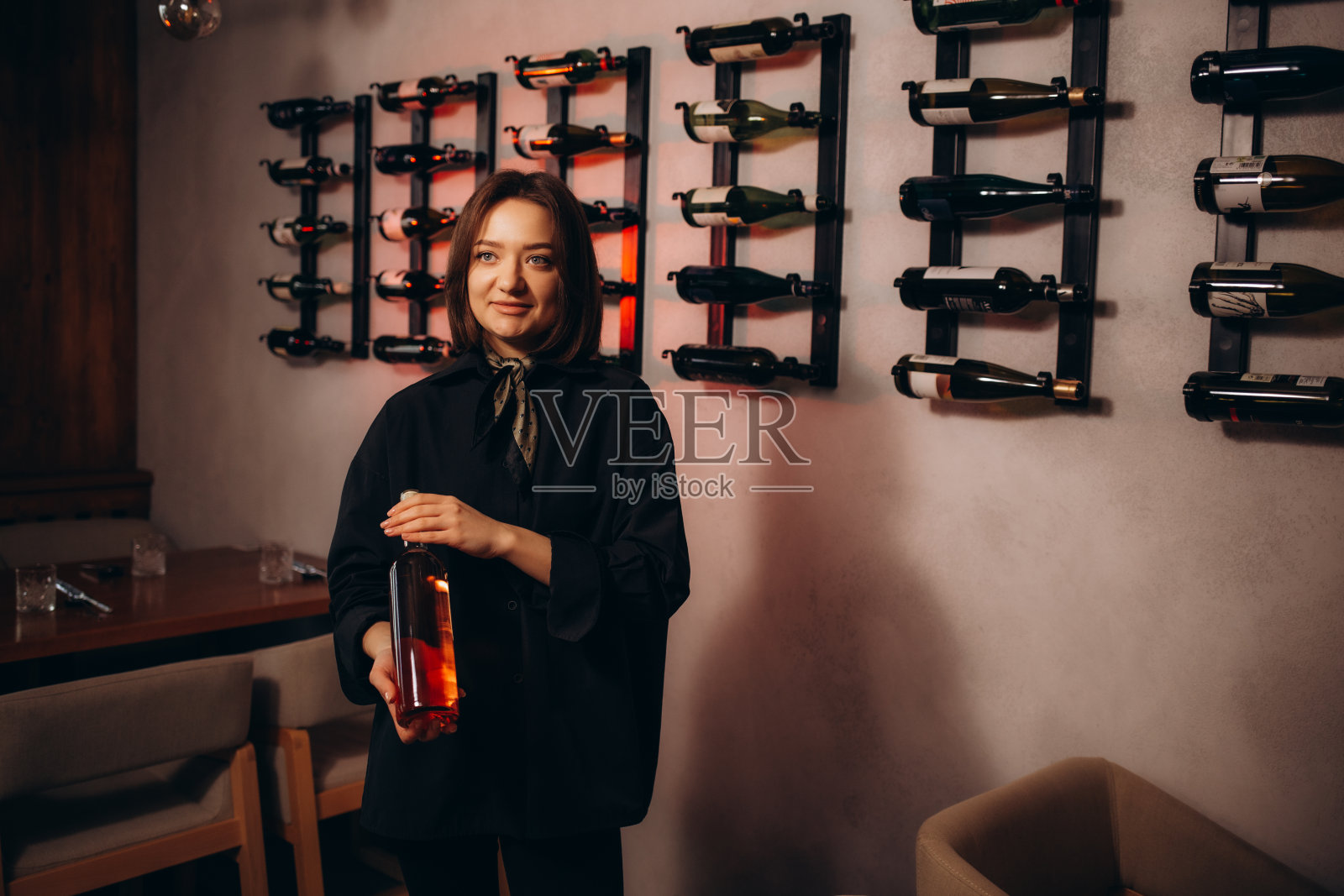 可爱的年轻酒品店员拿着并检查一瓶红酒的特写。那个女人站在旧地窖里微笑着照片摄影图片