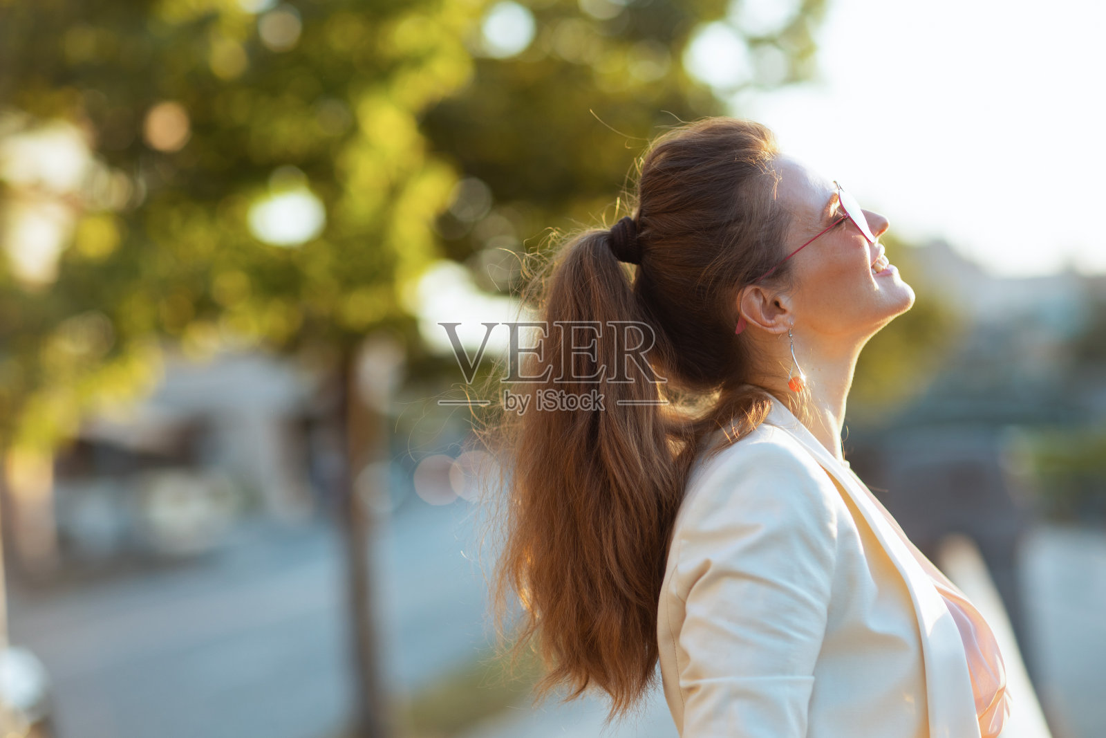 微笑优雅的女人在城市里穿着粉红色的裙子和白色的夹克照片摄影图片