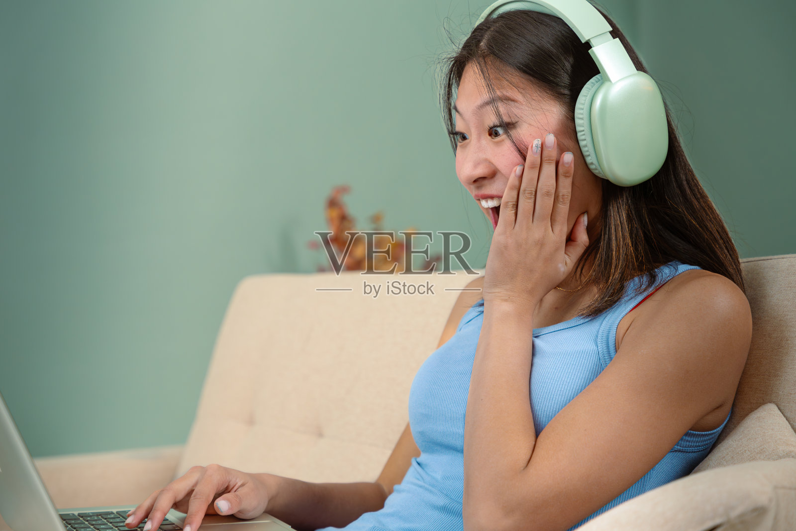 惊讶的中国年轻女子在家用笔记本电脑上网。照片摄影图片