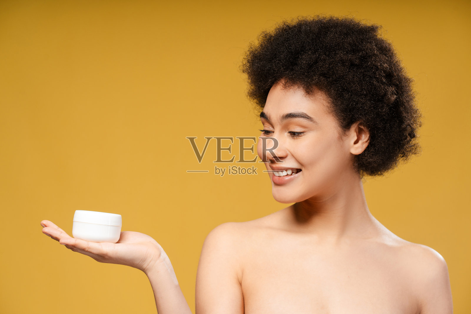 迷人的微笑拉丁女人卷发拿着一罐白色的保湿霜看向别处照片摄影图片