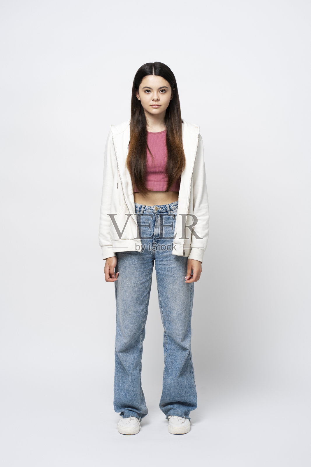 一个拉丁裔少女的肖像，穿着休闲的连帽衫，在灰色的背景上看着孤立的相机照片摄影图片