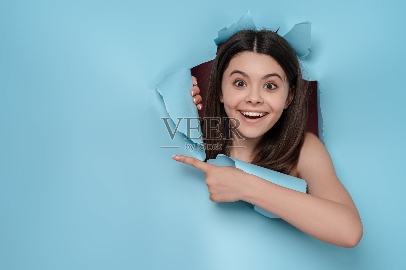 兴奋的黑发少女的肖像看着撕裂的背景，手指在复制空间照片摄影图片