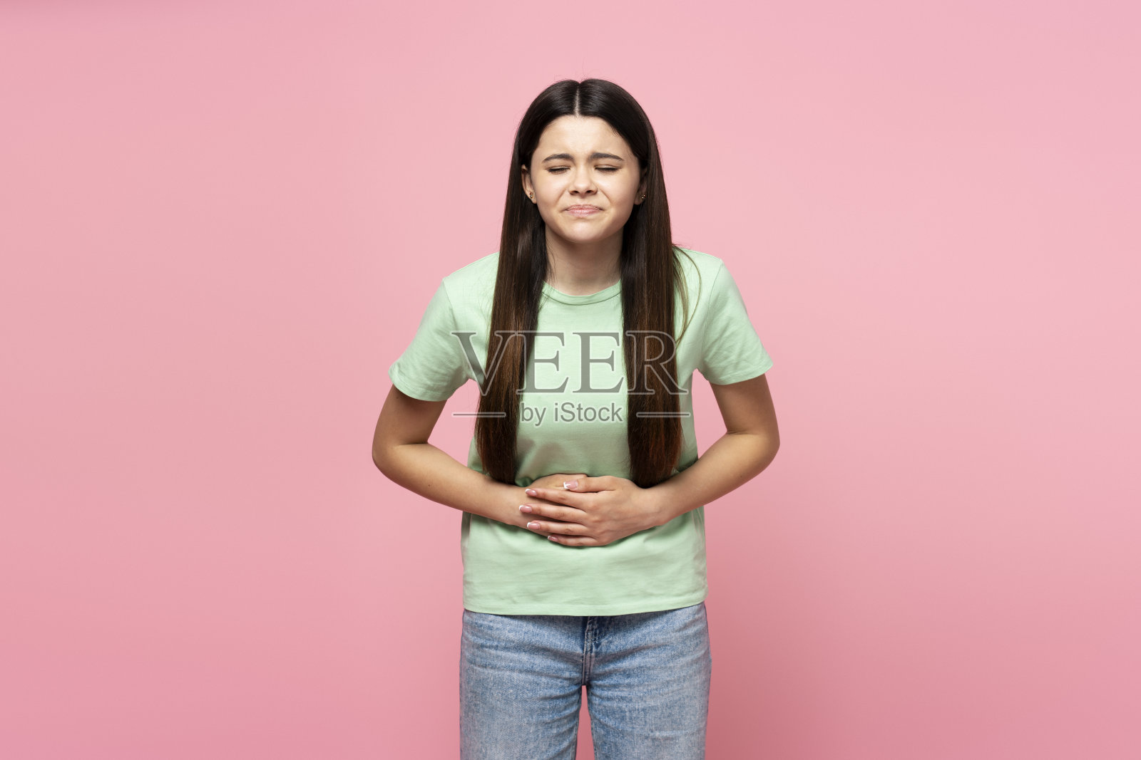 美丽的拉丁少女抱着肚子，肚子疼，孤立地站在粉红色的背景上照片摄影图片