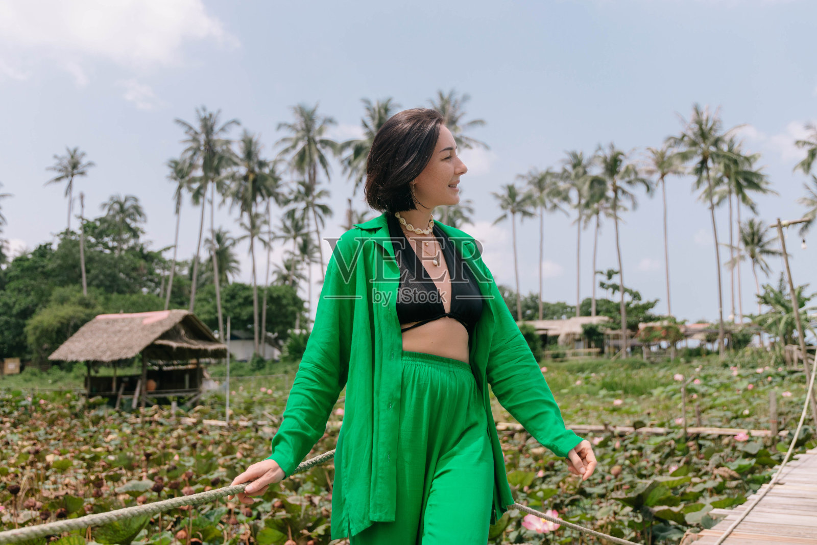 一个微笑的女人站在荷塘旁的木栈道上，背景是棕榈树照片摄影图片