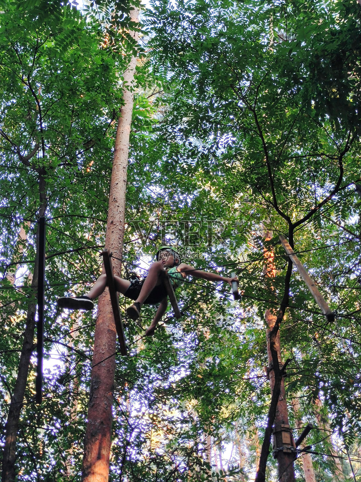 一个十几岁的男孩在游乐园的绳索公园里在悬挂的扶手上移动。从下面看照片摄影图片