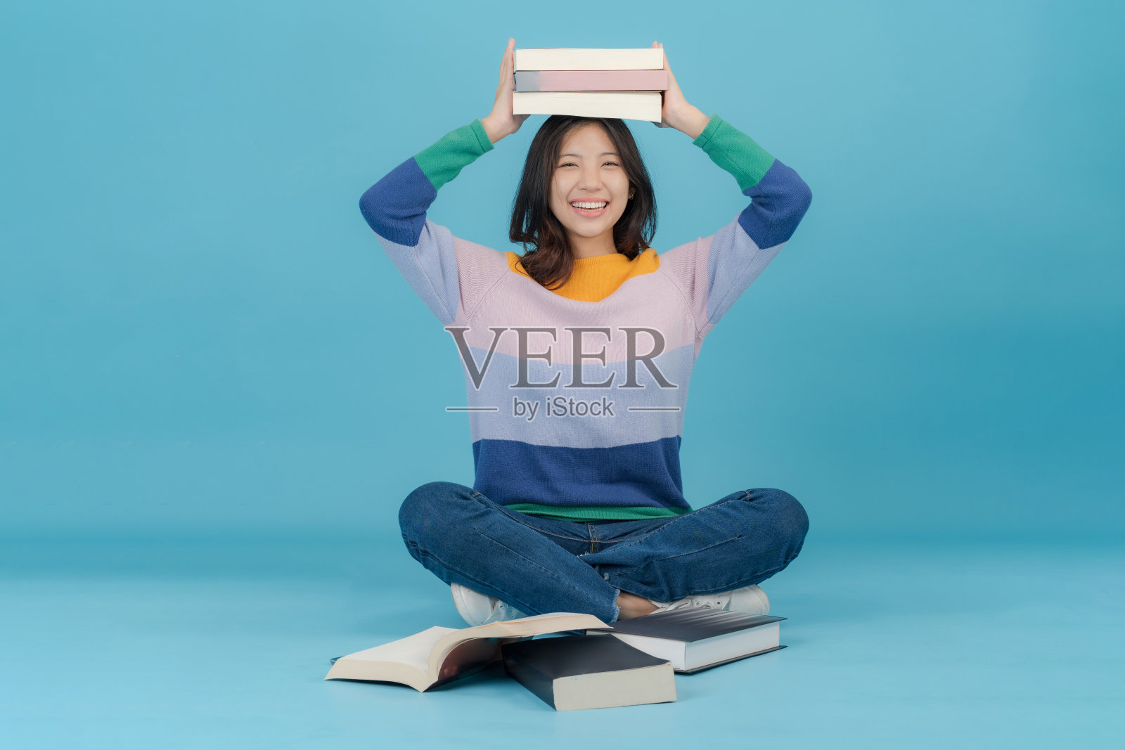 一位美丽的年轻女子愉快地微笑着，把许多书举在头上照片摄影图片