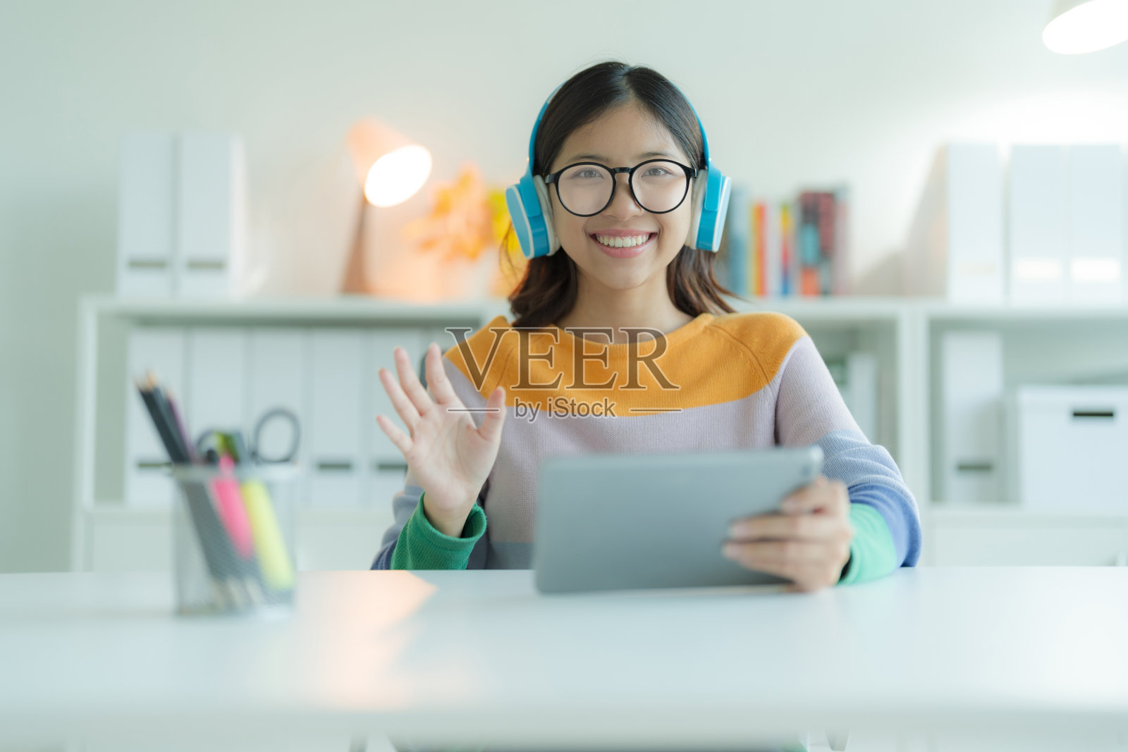 戴着眼镜和耳机在图书馆使用平板电脑的年轻女性或学生。她面带微笑，看起来很开心。照片摄影图片