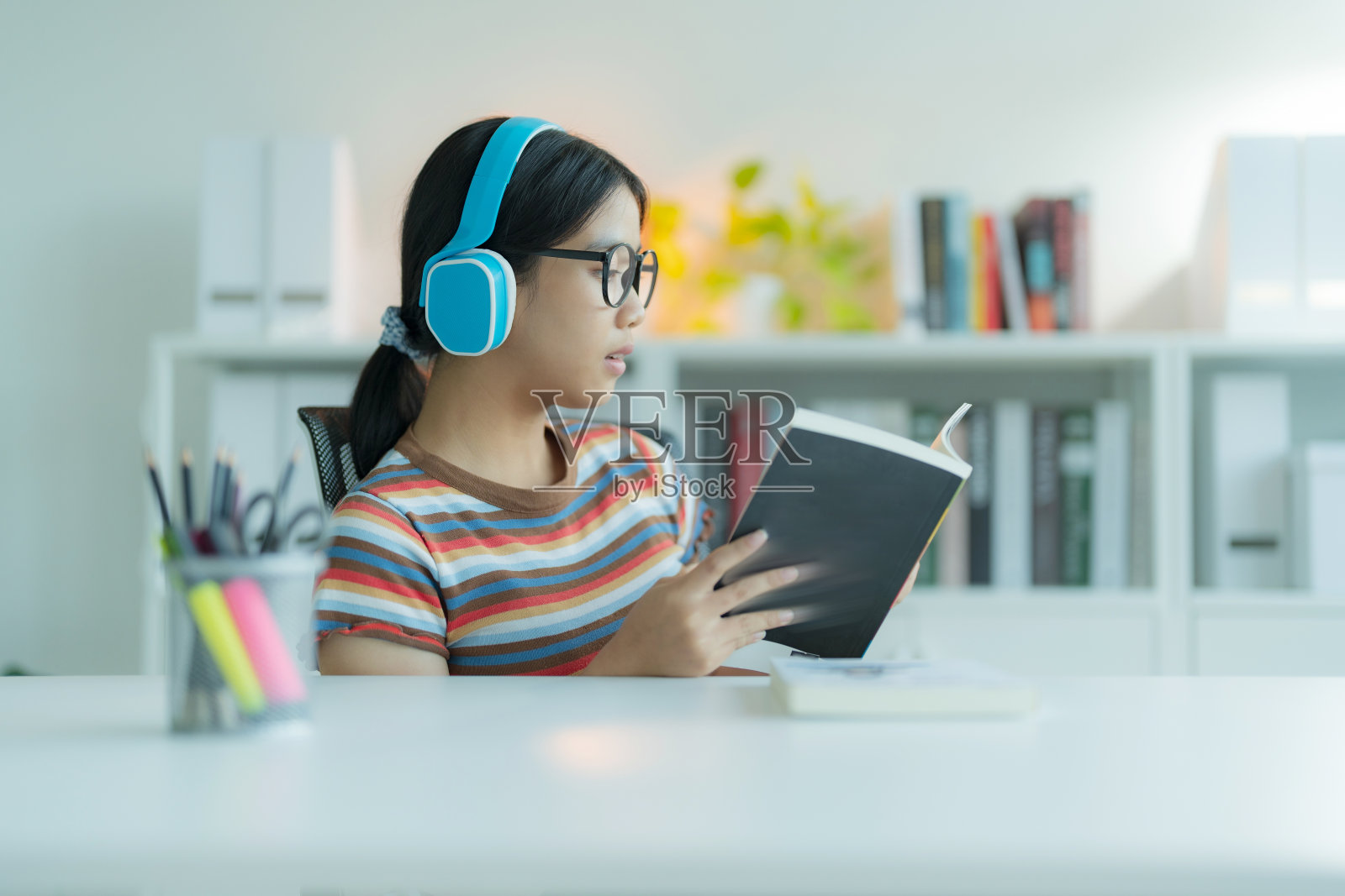 一个年轻的女孩或学生在图书馆戴着眼镜，她微笑着，看起来很开心。照片摄影图片