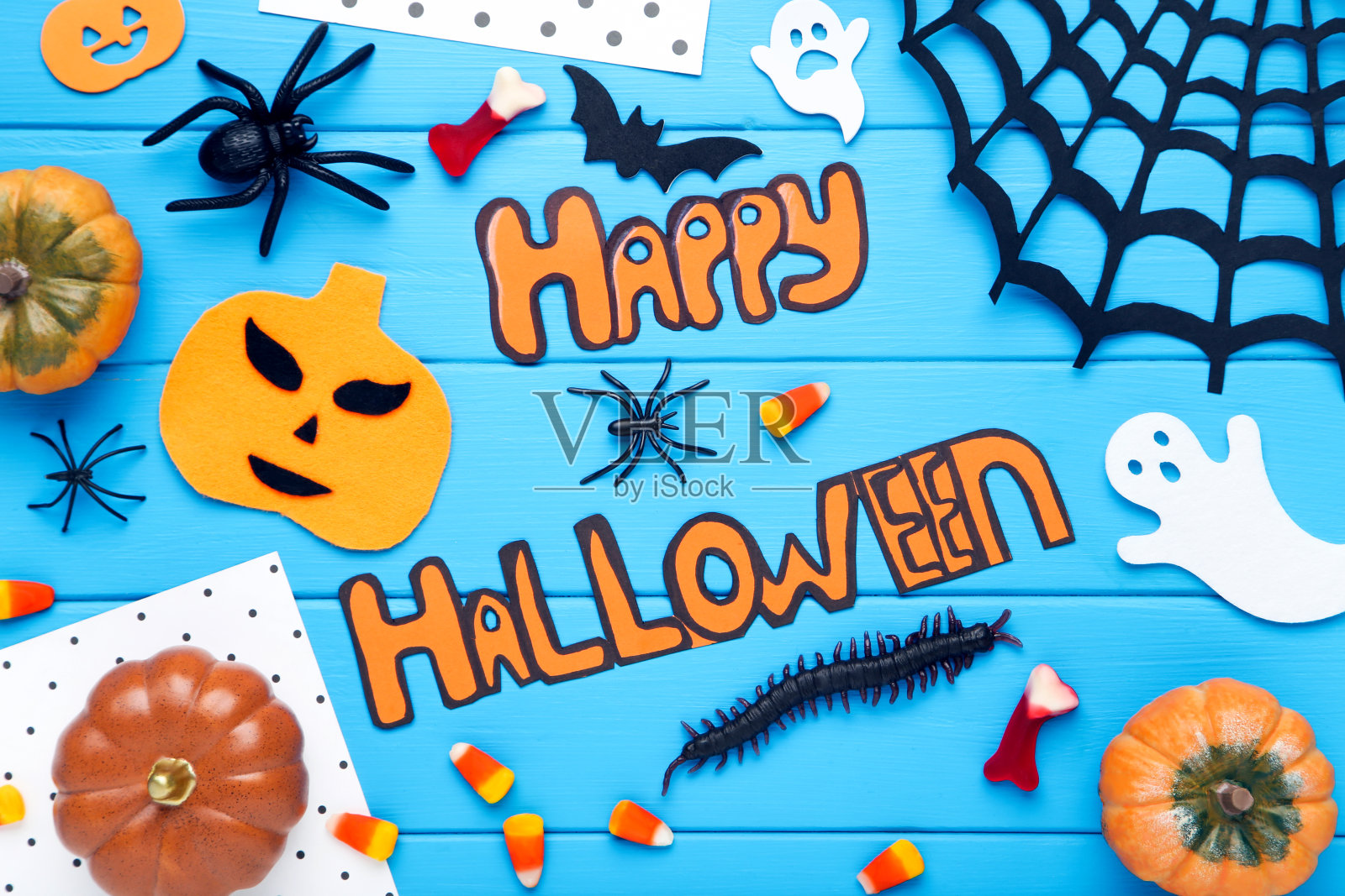 文字快乐万圣节与糖果，南瓜，蜘蛛和纸蝙蝠，鬼魂在蓝色的木制背景照片摄影图片
