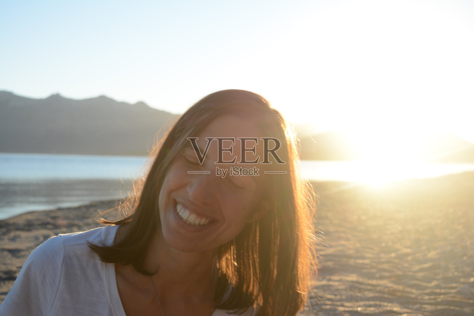 微笑的黑发长发女人独自在日落的海滩和湖边度假照片摄影图片