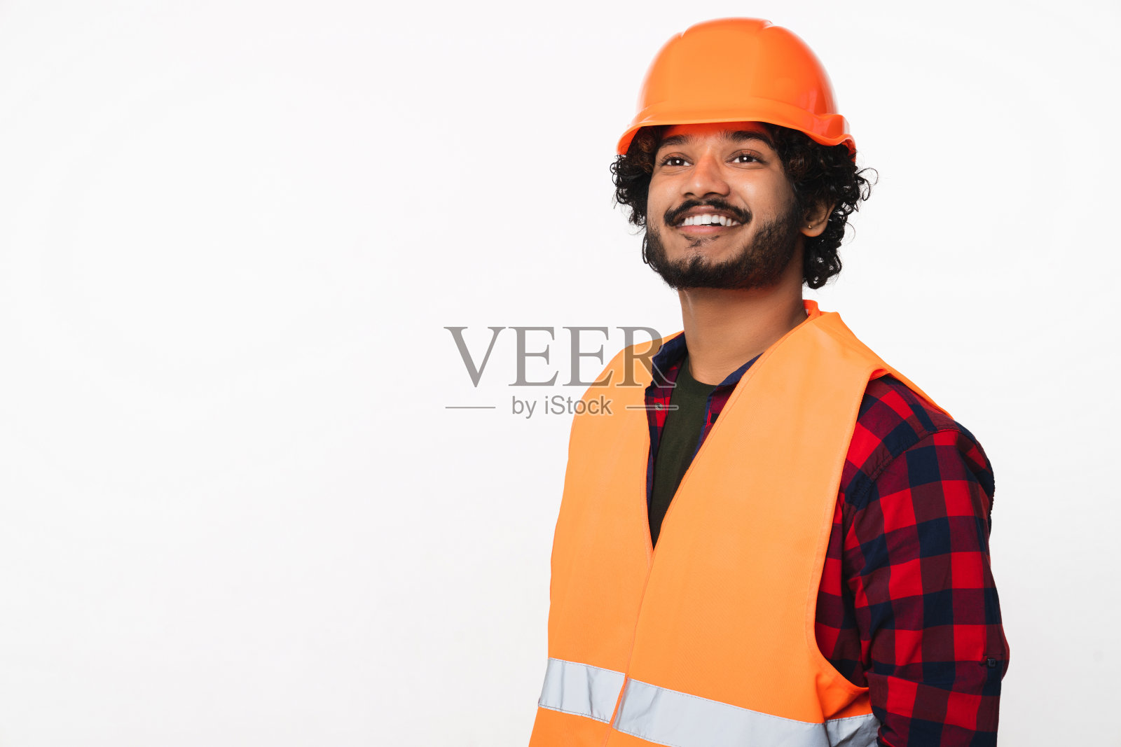 快乐的年轻印度建筑工人戴着头盔，穿着橙色制服，孤立在白色的背景上照片摄影图片