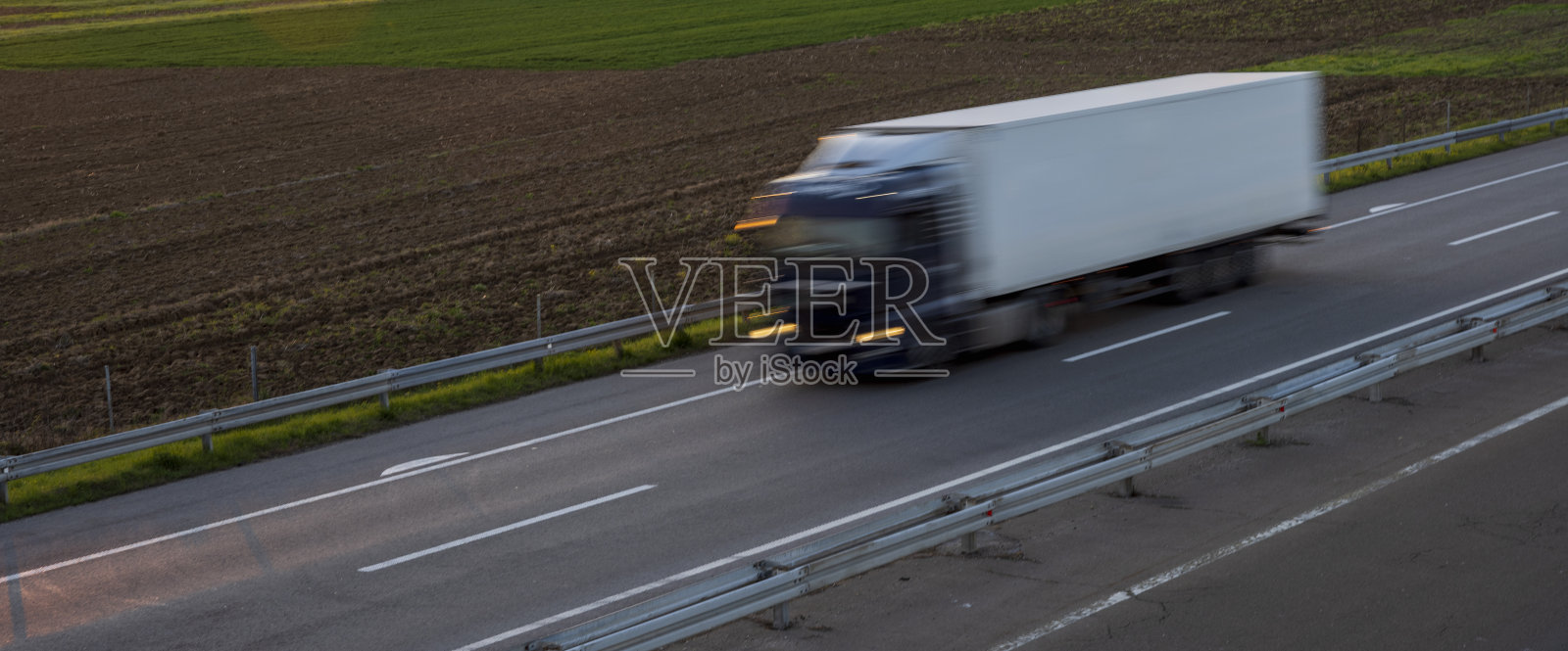 卡车在公路上高速行驶，穿过乡村风景。高速公路高速行驶。高速公路上超速行驶的景象。背景是美丽的日落。照片摄影图片