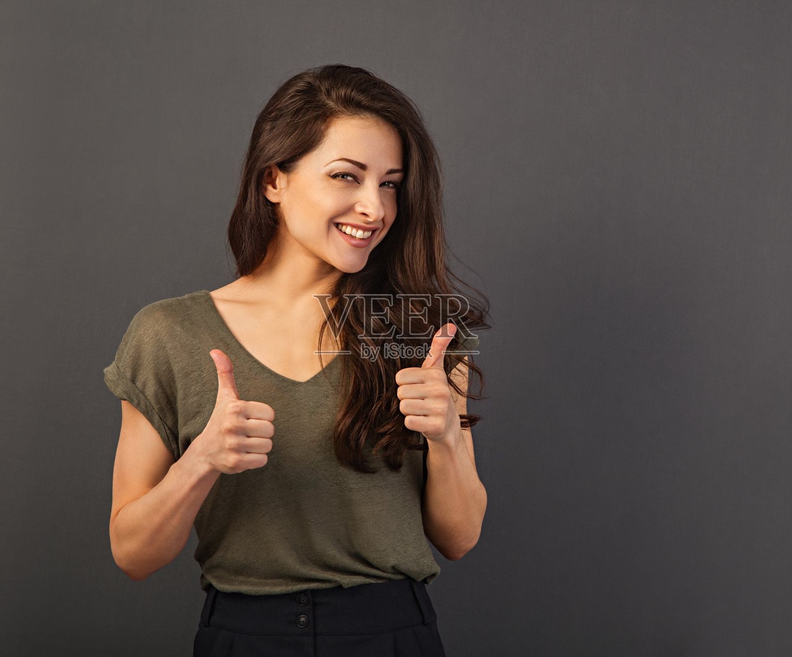 漂亮的商人，长着牙齿，微笑着，棕色健康的长发，站着，两只手竖起大拇指。健康的生活方式和成功的事业。正面特写照片摄影图片