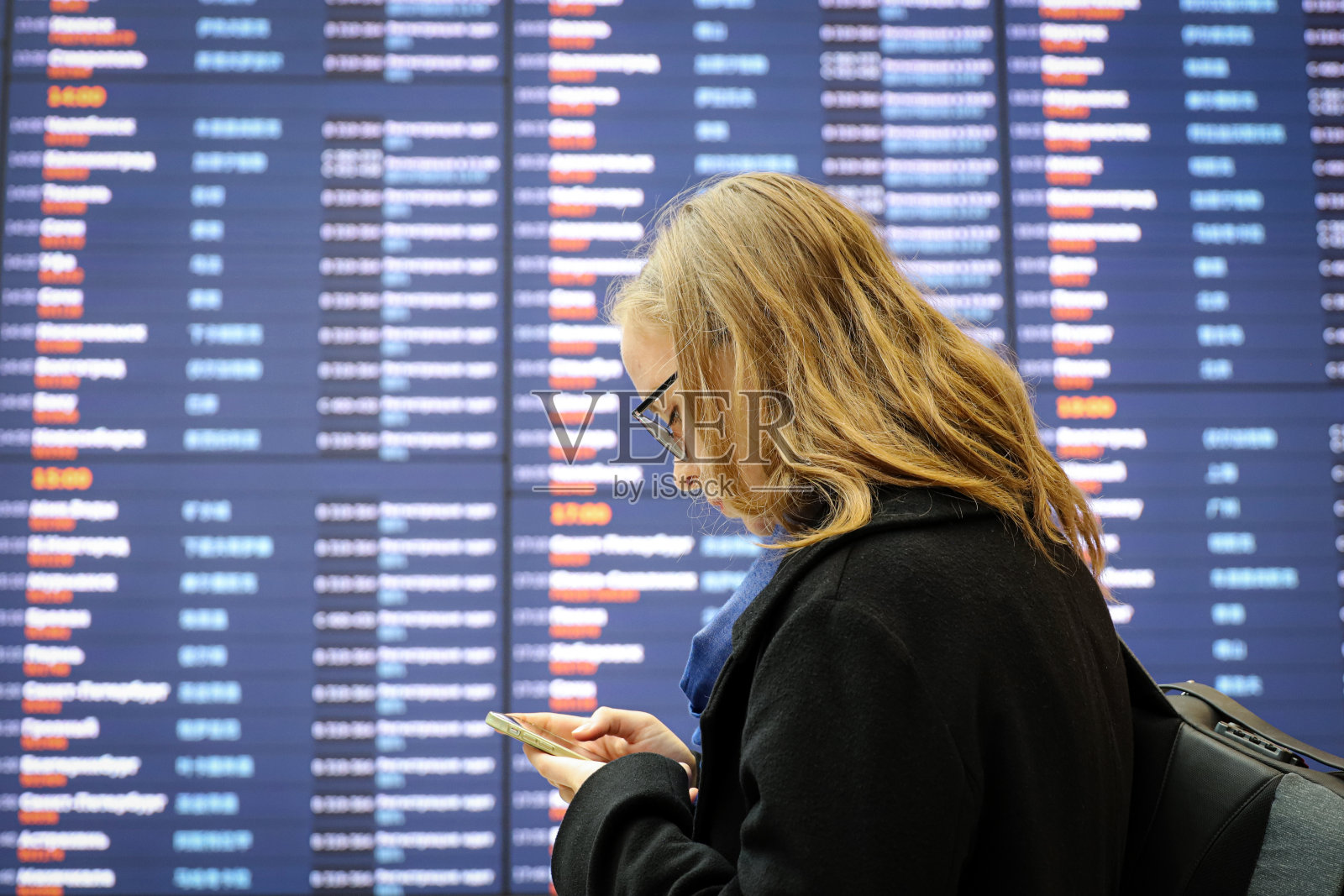 在莫斯科谢列梅捷沃机场，女孩拿着智能手机站在离港信息牌旁照片摄影图片