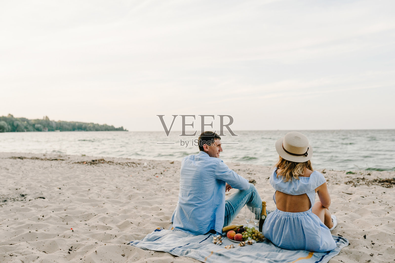 一男一女正在野餐约会。一对夫妇坐在沙滩上野餐的后视图。女性和男性在海滩上享受阳光明媚的夏日。共度时光。后视图照片摄影图片