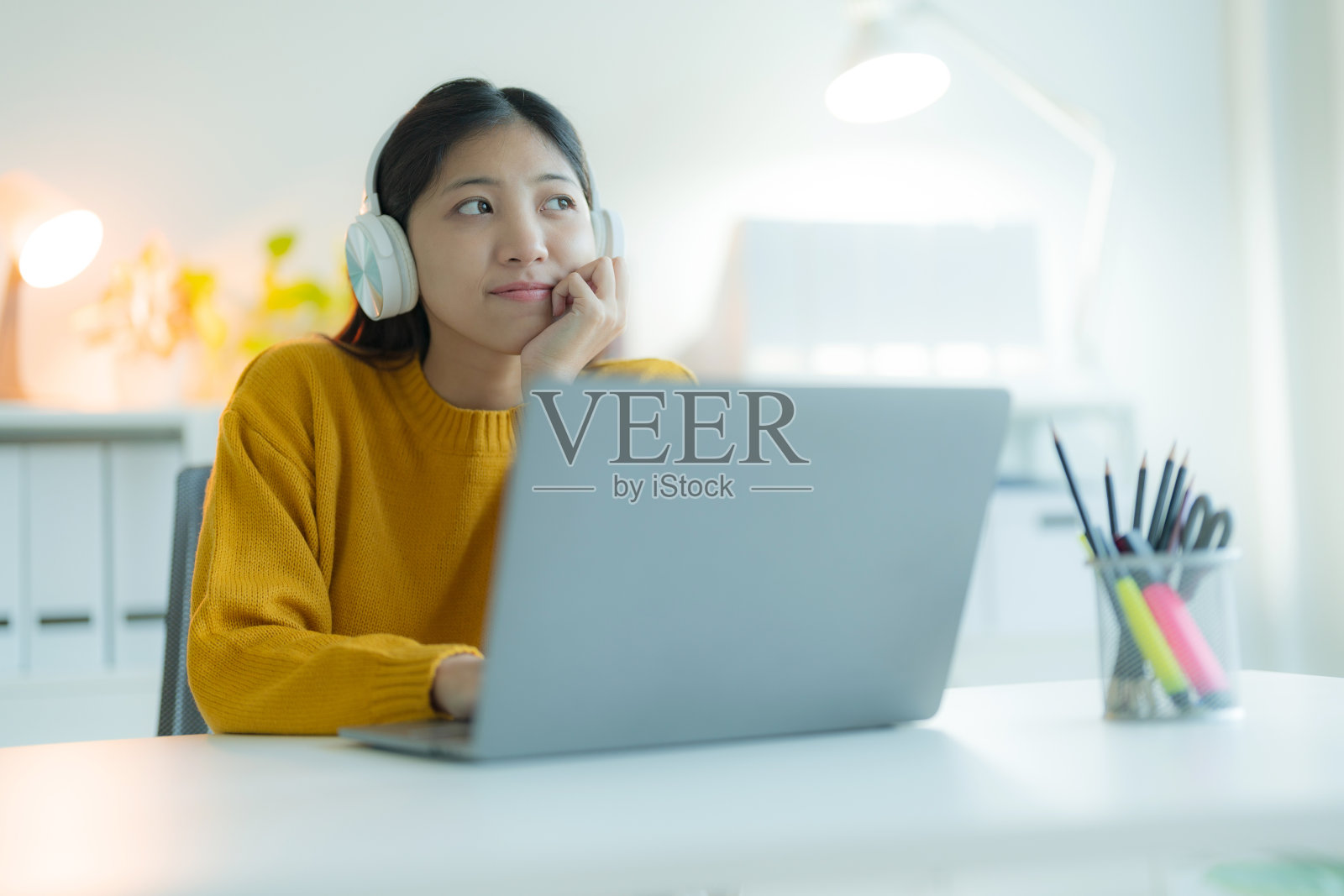 一位迷人的年轻女子在她的家庭办公室里戴着耳机使用笔记本电脑，微笑着，看起来很开心照片摄影图片