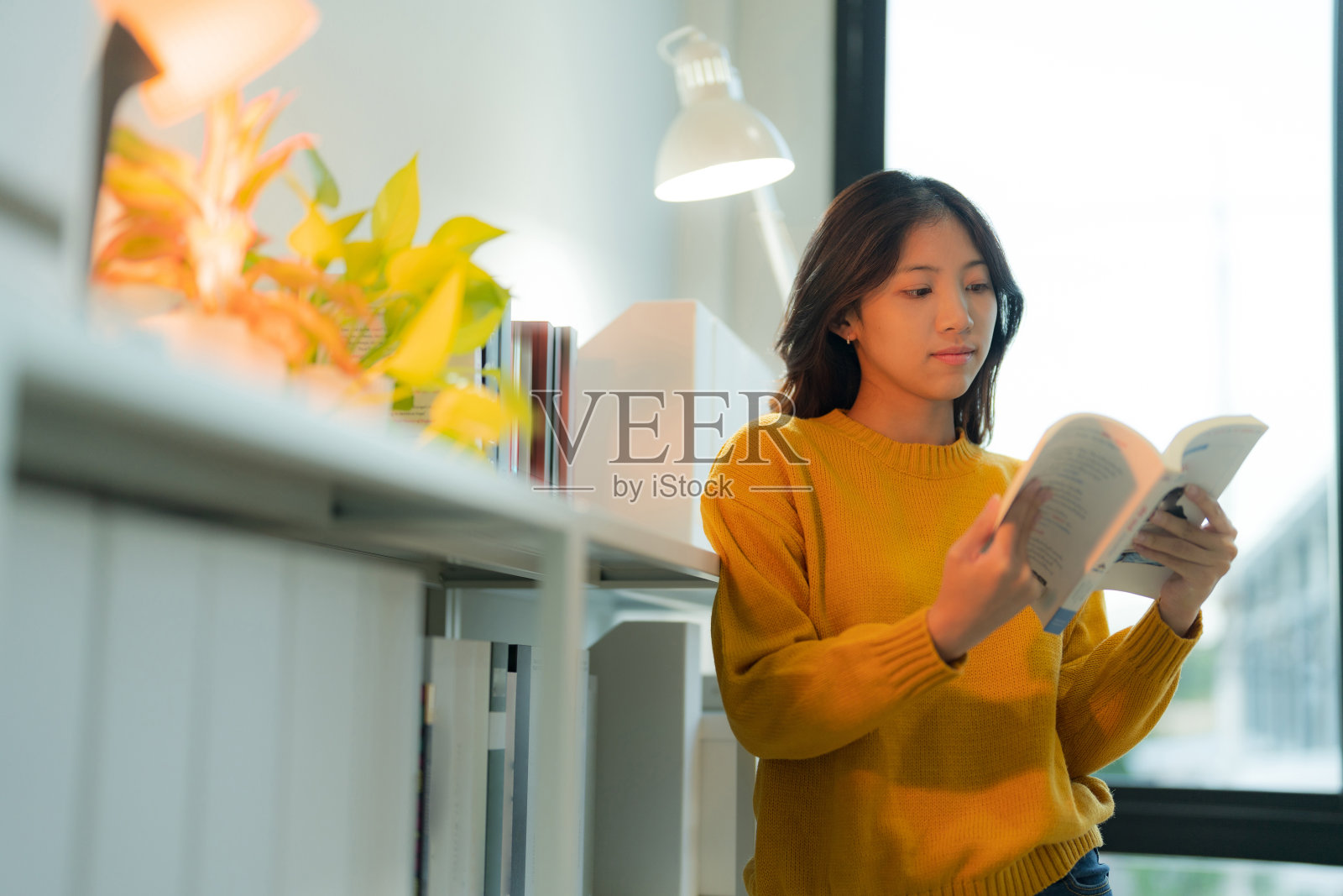 在她的家庭办公室里，一个年轻迷人的女人微笑着读着书，看起来很满足照片摄影图片