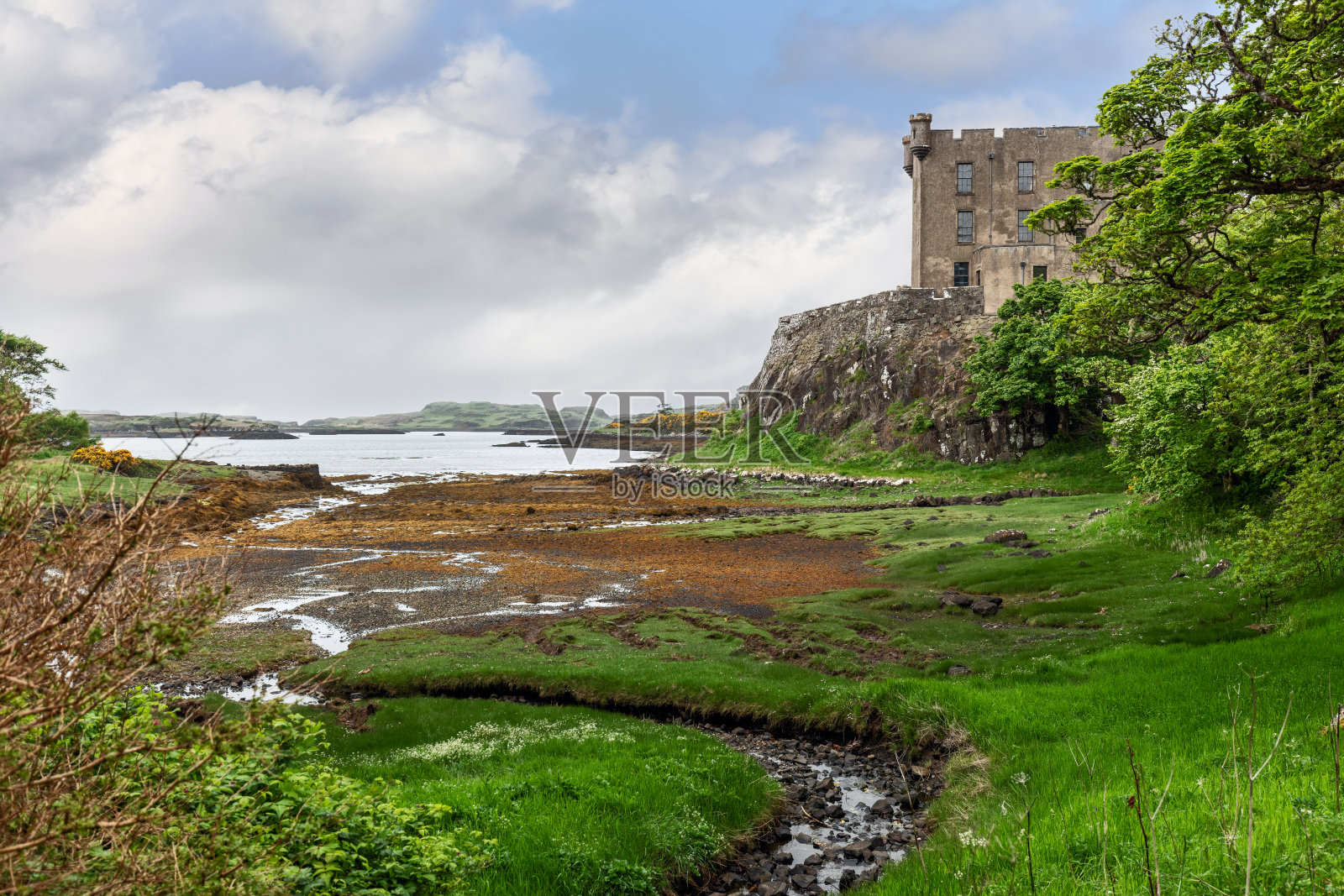 位于斯凯岛的历史悠久的Dunvegan城堡，由充满活力的绿色植物和鹅卵石海岸线组成，在充满活力的天空下，唤起苏格兰丰富的遗产照片摄影图片