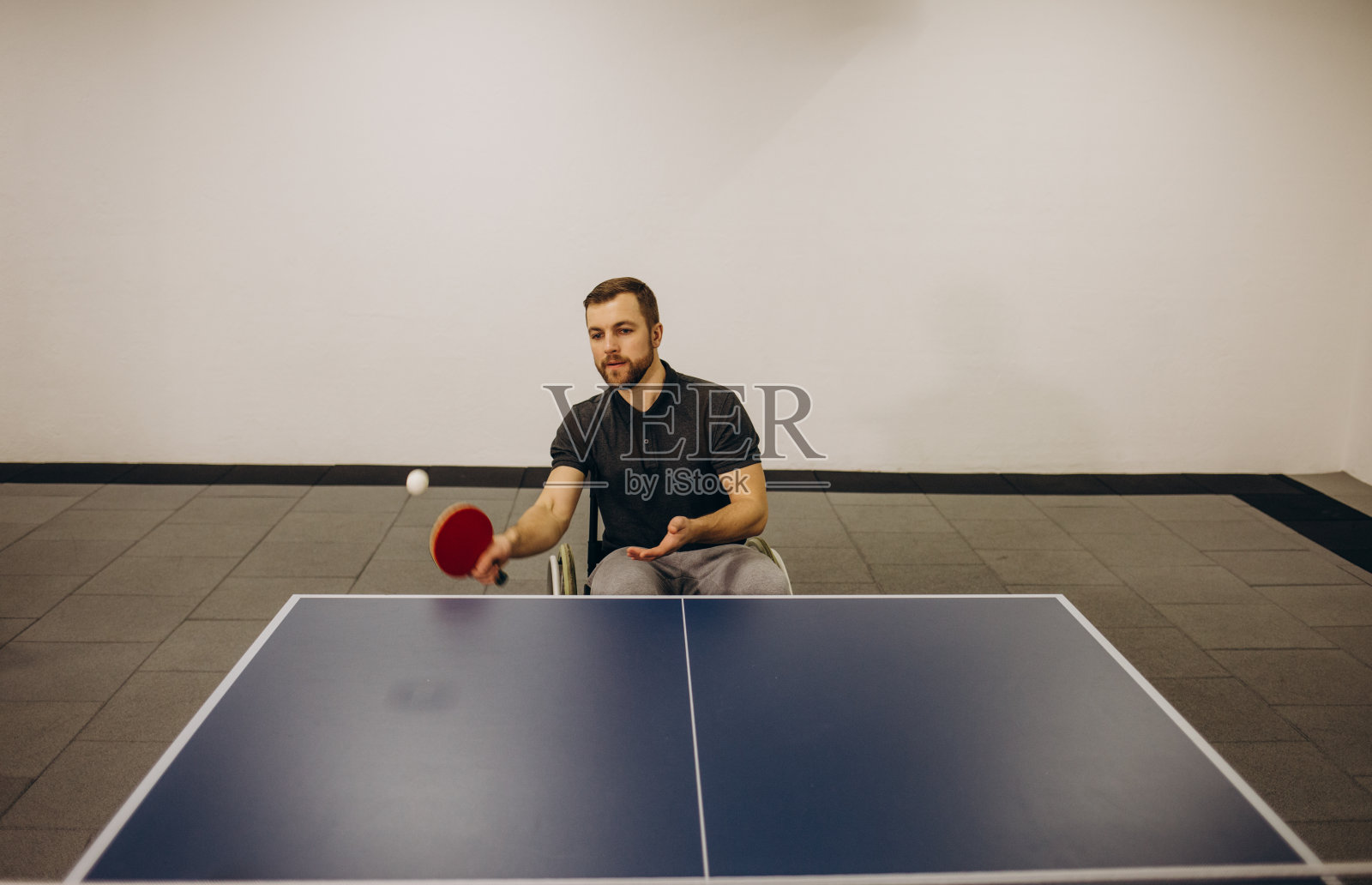 一个坐在轮椅上的年轻英俊的男子正在打乒乓球。照片摄影图片