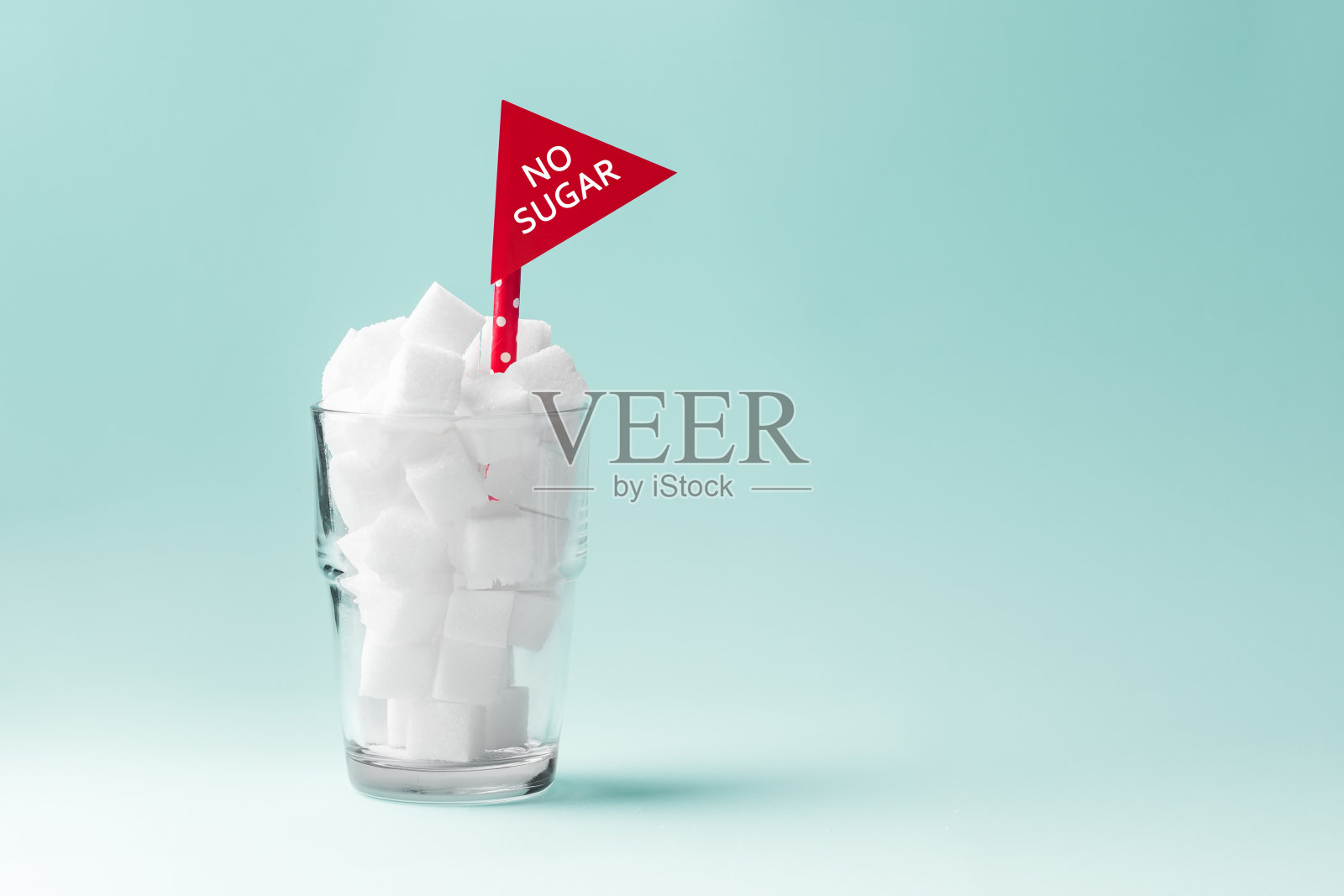 玻璃杯里装满了没有糖的方糖，绿色背景上有红色的标志照片摄影图片