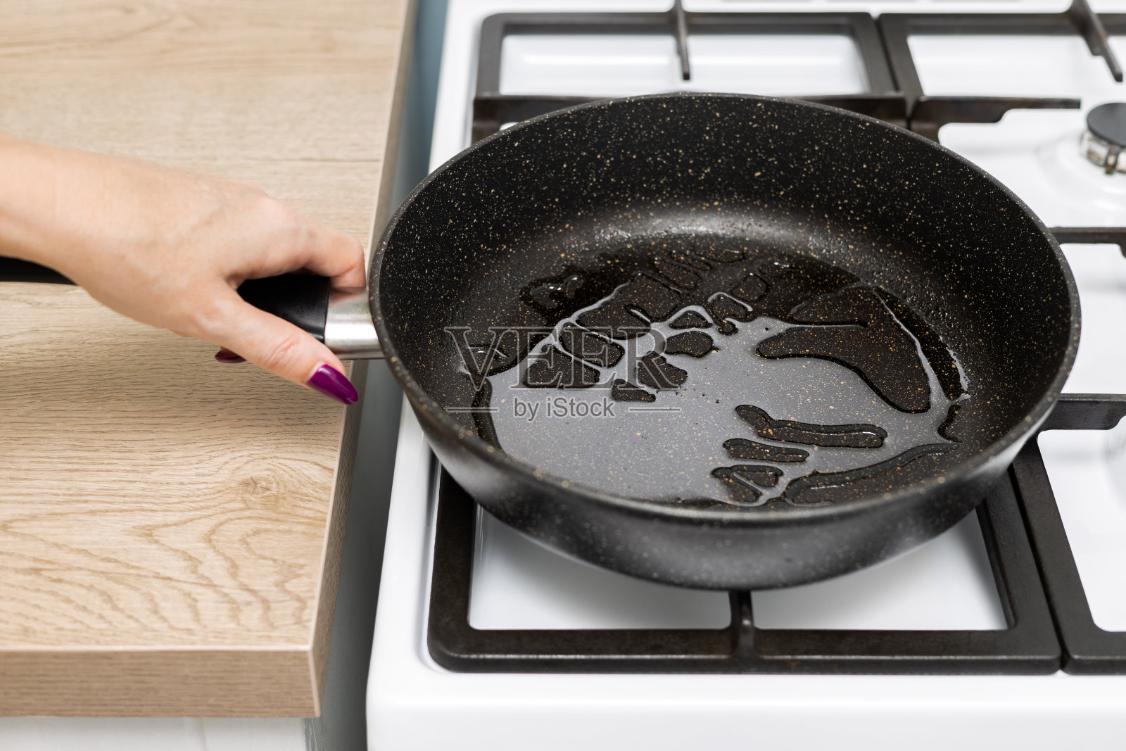 家庭主妇把油倒进煎锅里。照片摄影图片