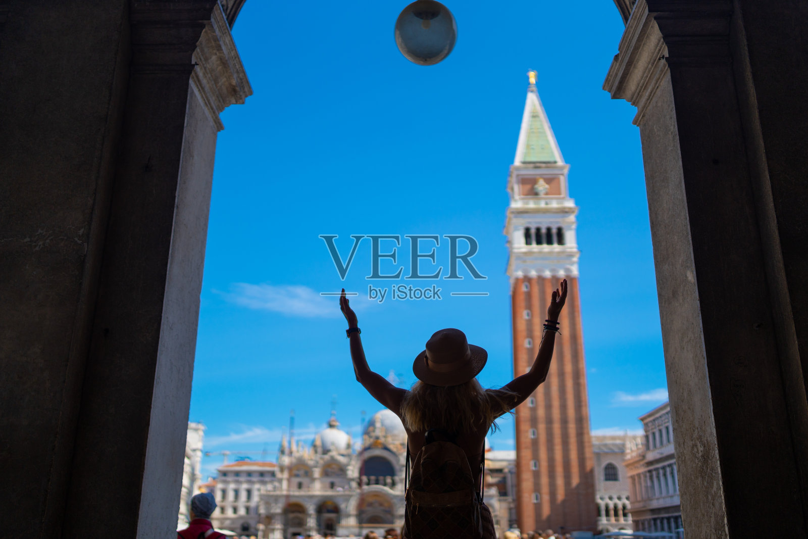 一名女子站在意大利威尼斯的圣马可大教堂和钟楼前，伸开双臂照片摄影图片