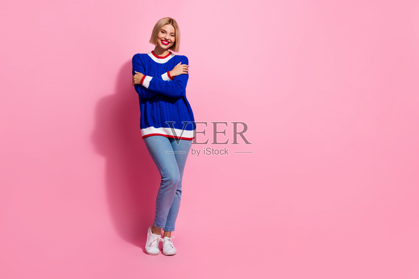 全身照片迷人的年轻金发女士在蓝色针织套头衫与牛仔裤享受她的风格孤立在粉红色的背景照片摄影图片