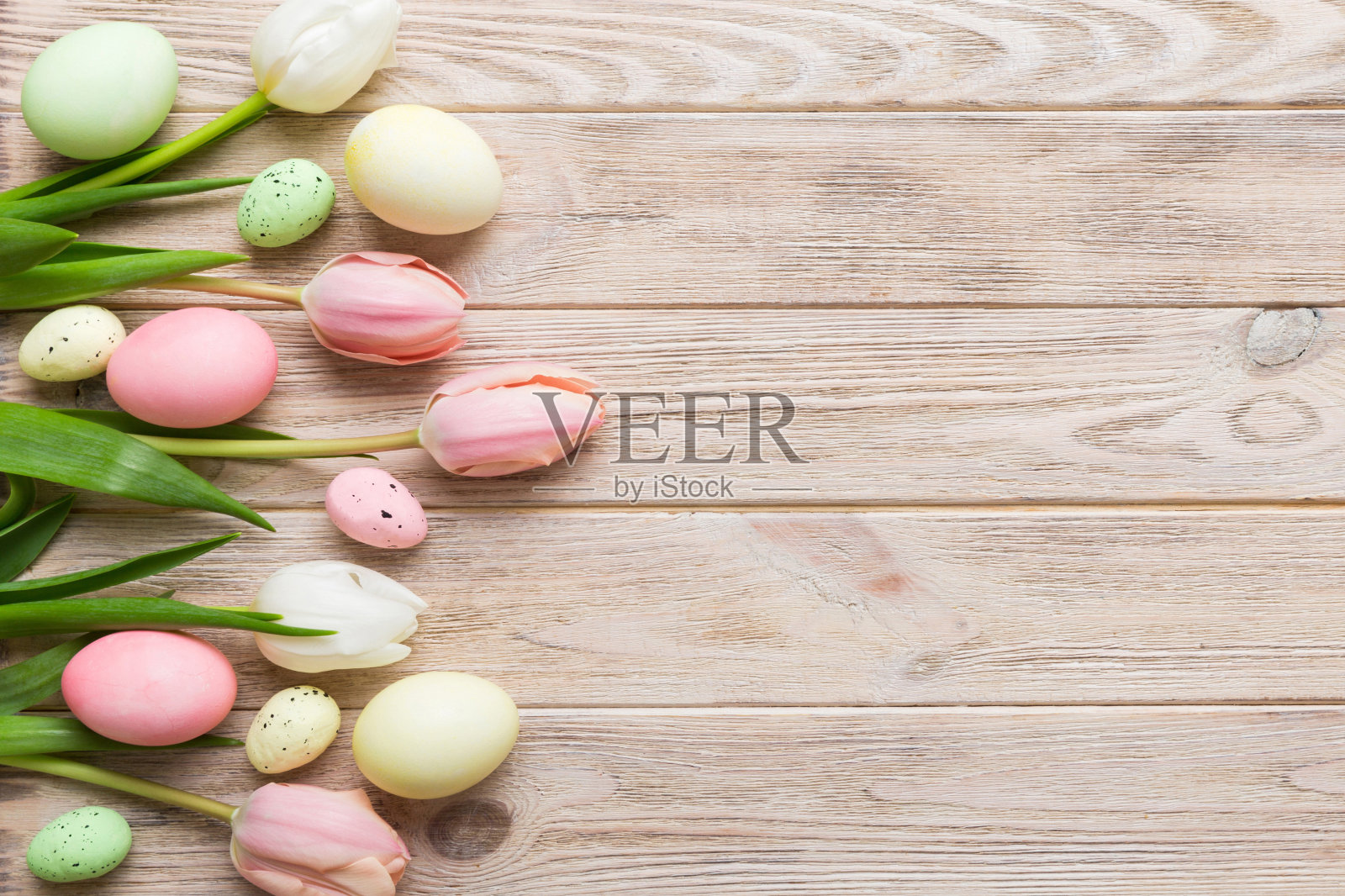 复活节作文快乐。复活节彩蛋在彩色的桌子上，黄色的郁金香。自然染色彩色鸡蛋背景顶视图与复制空间照片摄影图片