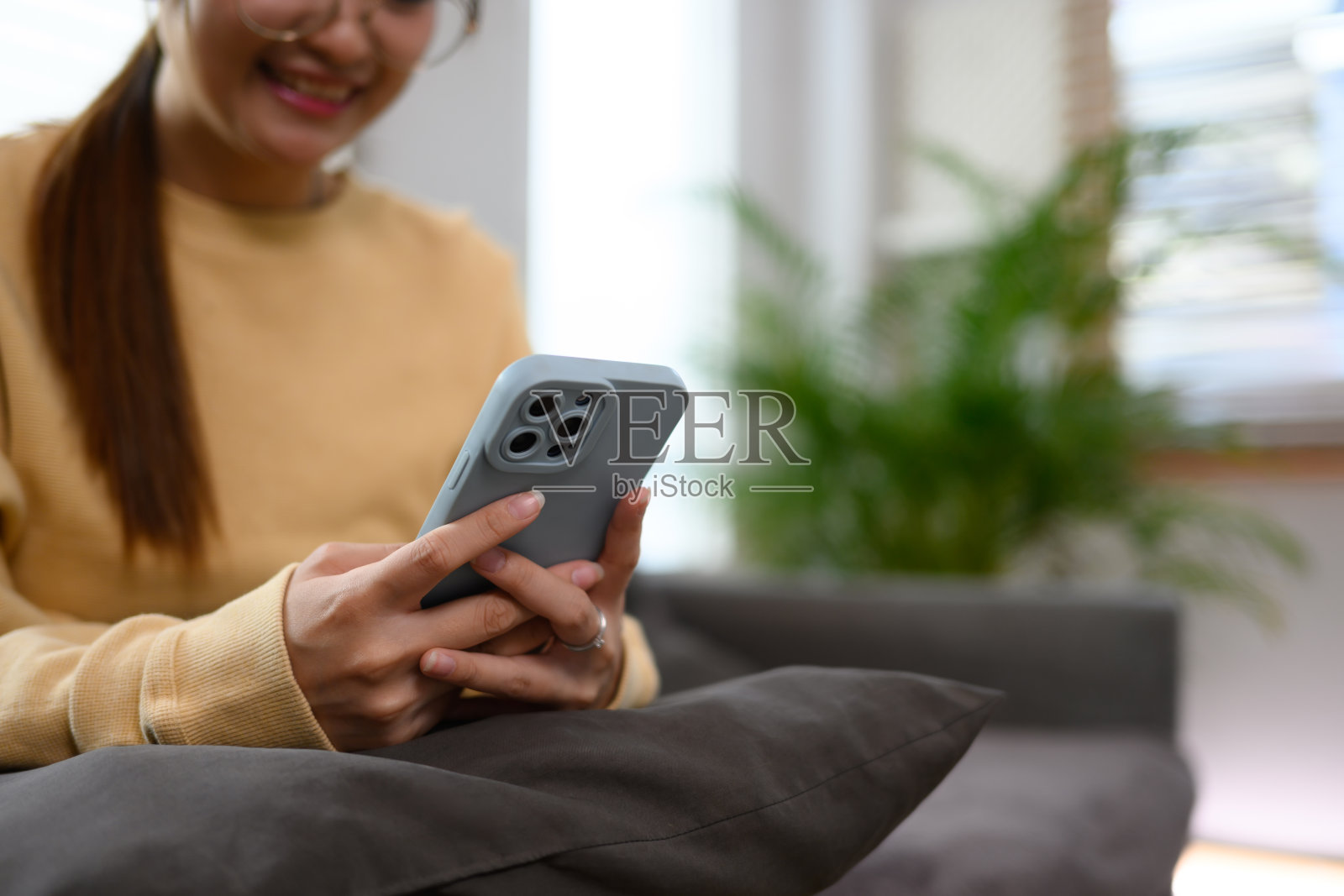 年轻女子坐在家里的沙发上，用手机打字的剪辑镜头照片摄影图片