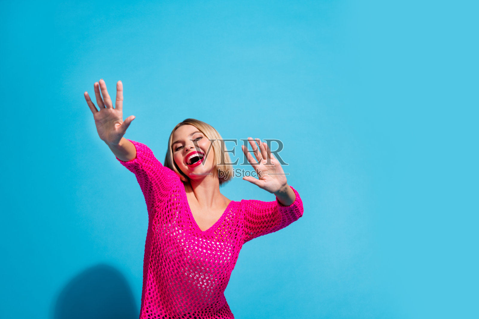 漂亮的年轻女孩的照片肖像跳舞寒心有乐趣穿着时尚的粉红色针织服装孤立的蓝色背景照片摄影图片