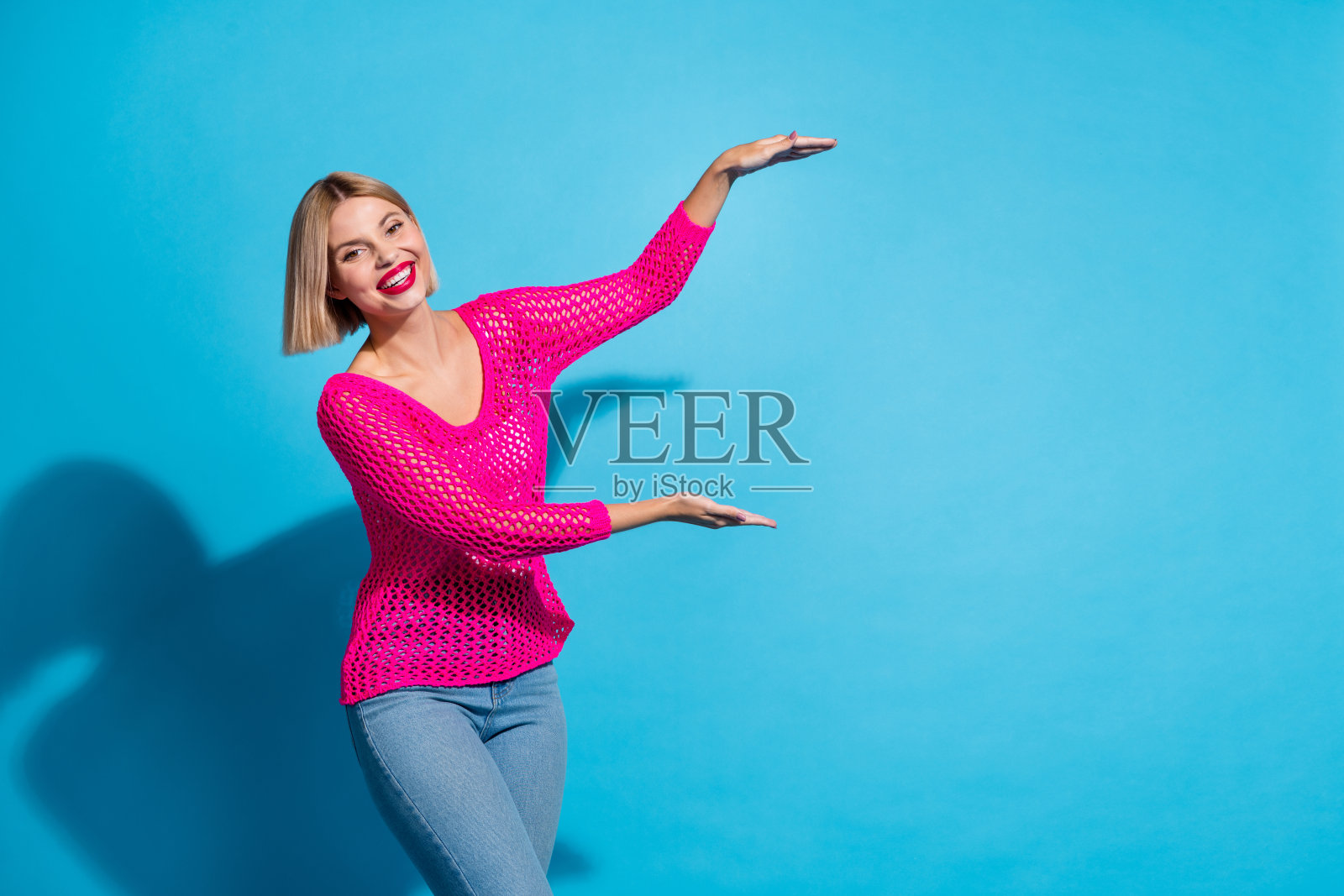 照片肖像可爱的年轻女士双手显示测量身高穿着时尚的粉红色针织服装孤立在蓝色背景照片摄影图片