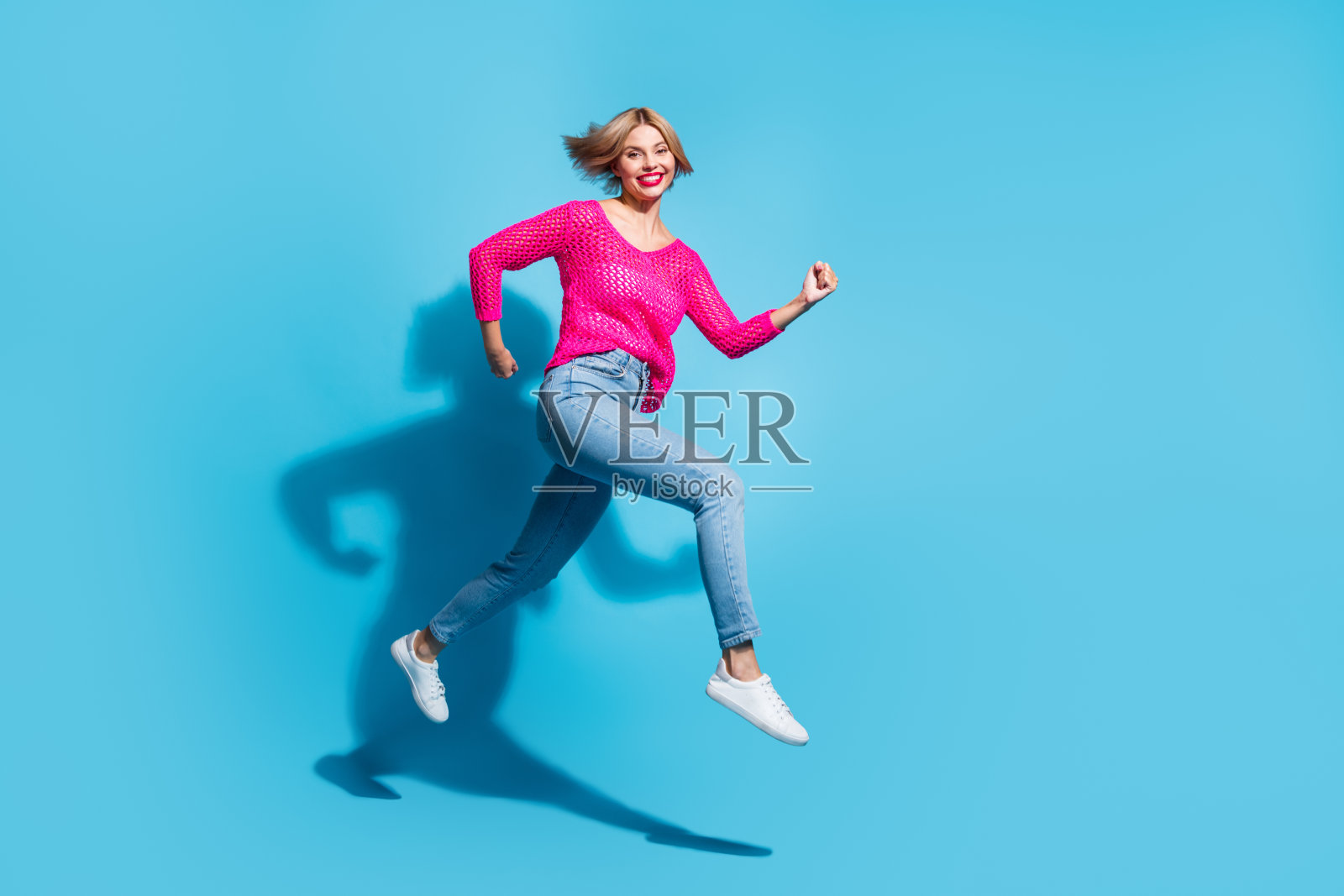 漂亮的年轻女孩的全尺寸照片跑得很快，有乐趣穿时髦的粉红色针织服装孤立的蓝色背景照片摄影图片