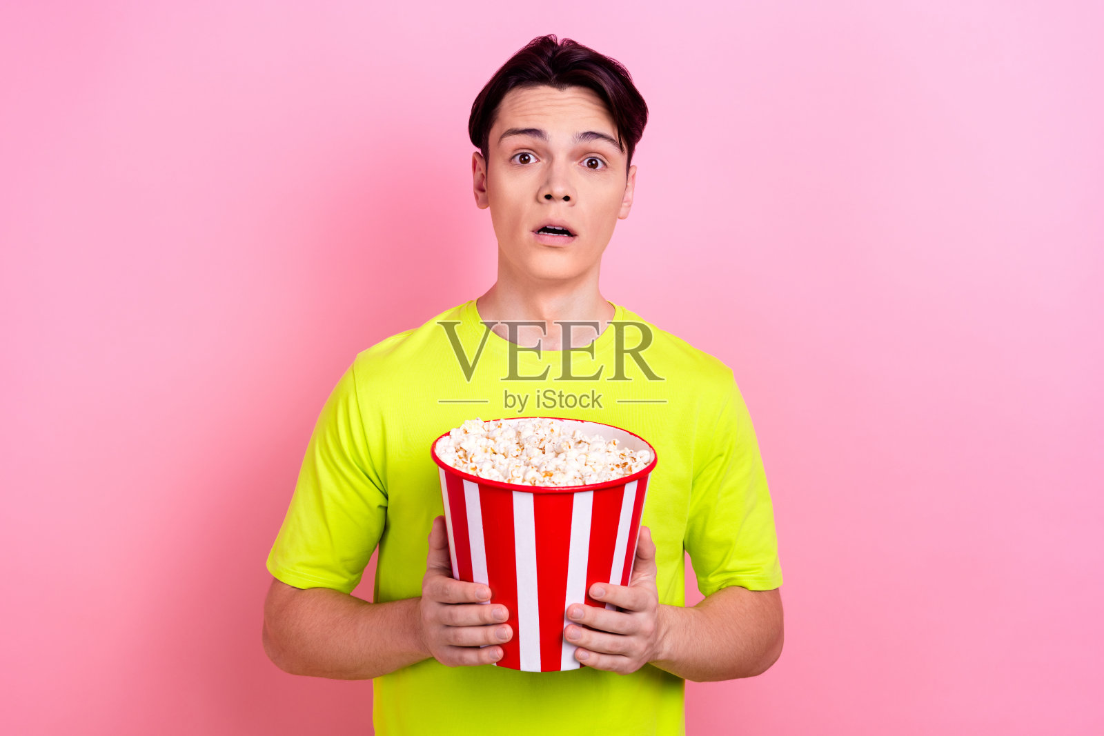 漂亮的少年男子的照片肖像拿着爆米花害怕看恐怖穿着时髦的黄色衣服孤立在粉红色的背景照片摄影图片