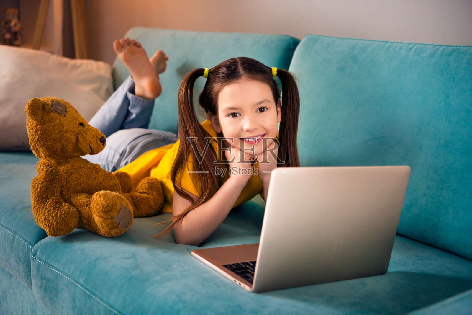 可爱小女孩的照片肖像躺在沙发上休息看电影卡通穿着时髦的黄色衣服现代娱乐室内部照片摄影图片