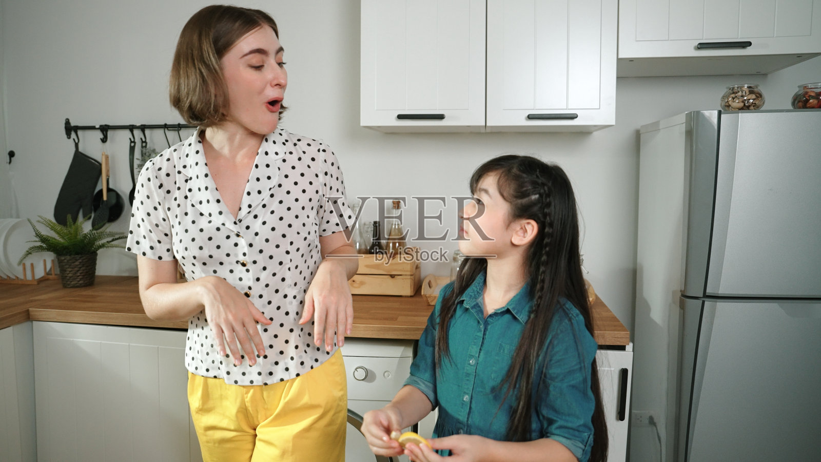 白人母亲和亚洲女孩一起做饭，吃橘子。教育学。照片摄影图片