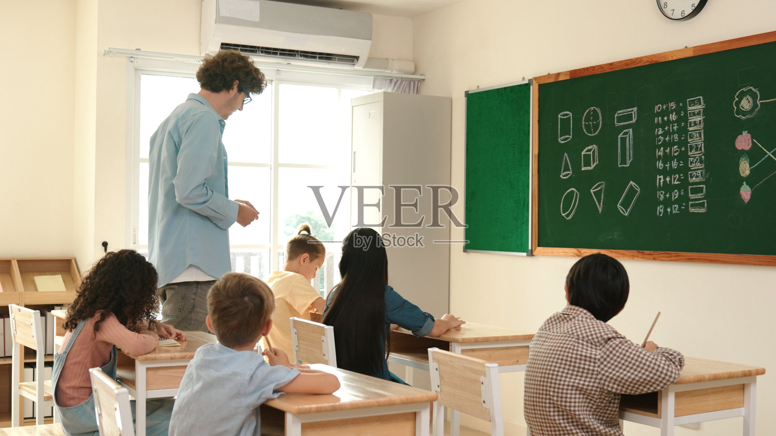 聪明的老师一边看着学生的作业一边走在教室里。教育学。照片摄影图片