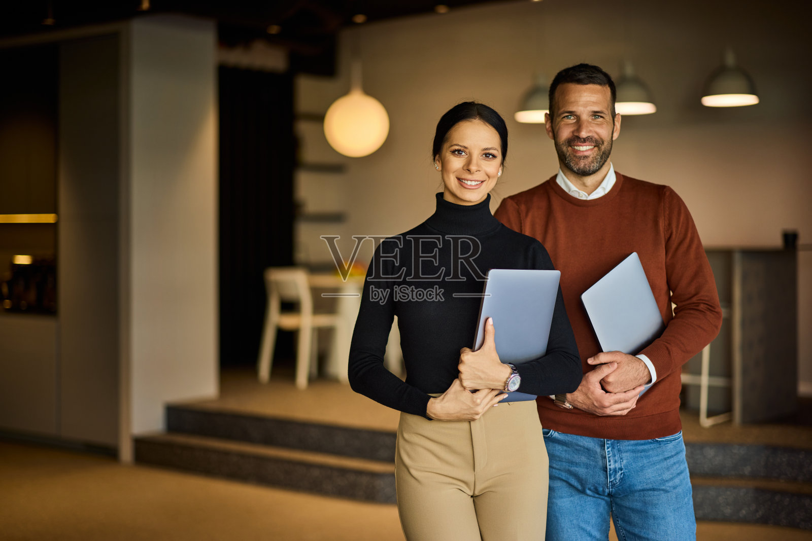 商人们站在办公室里，手里拿着笔记本电脑，对着镜头微笑。照片摄影图片