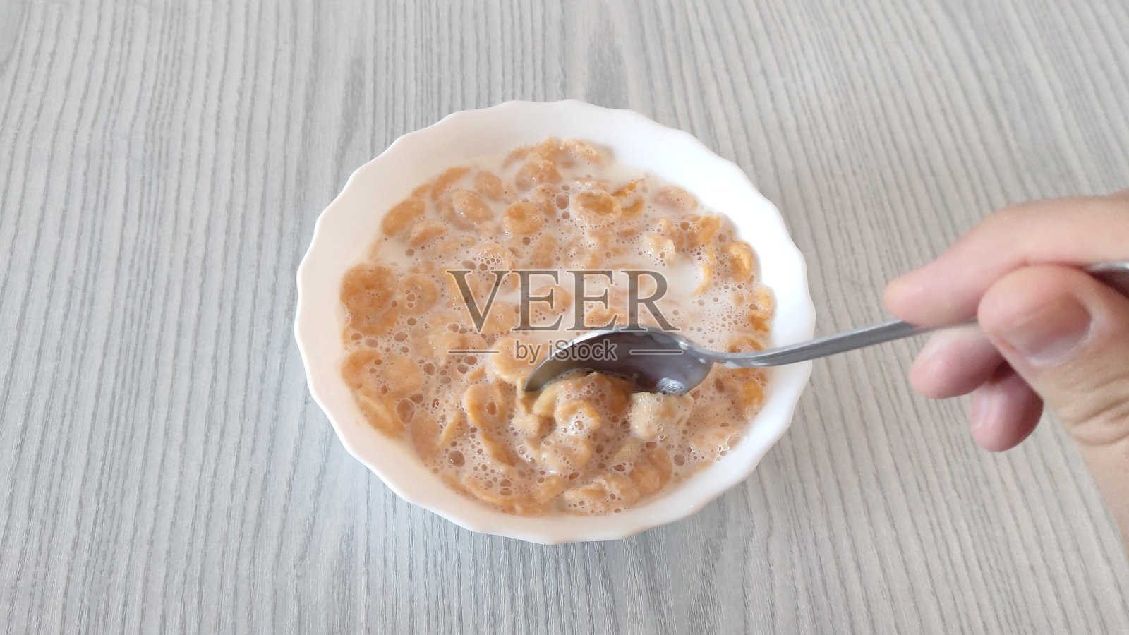 男人用勺子在盘子里搅拌玉米片和牛奶照片摄影图片