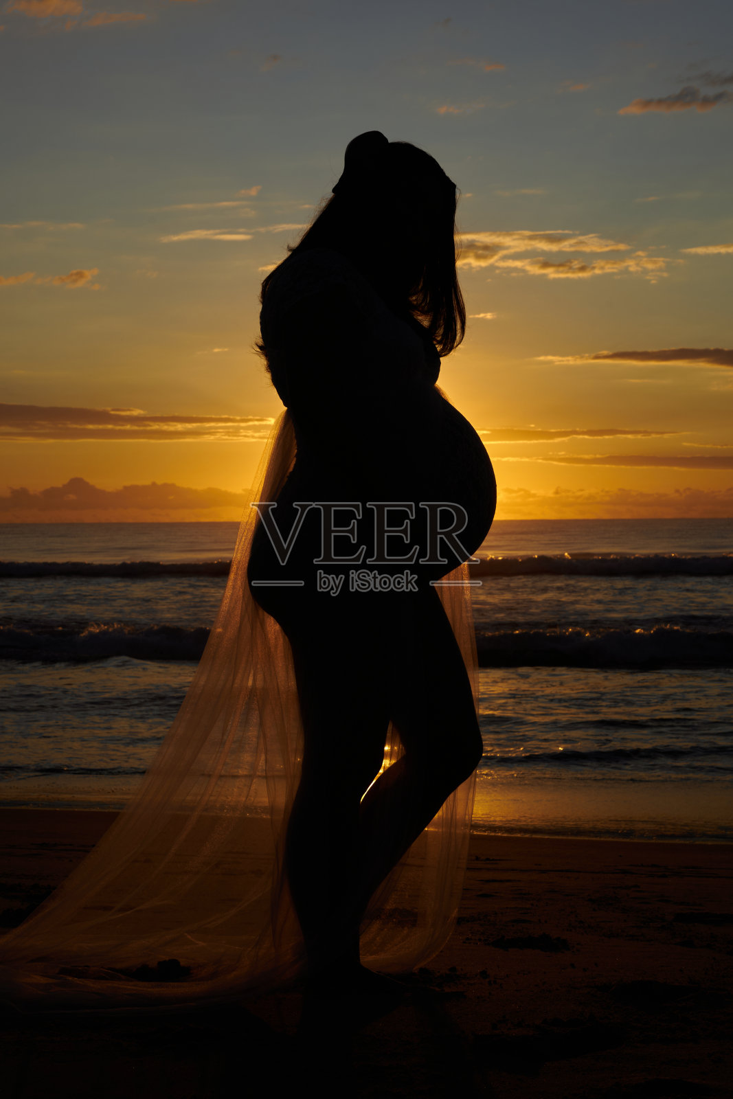 孕妇在日出或日落时拍摄，孕妇在海滩上放松，在海滩旁边的冲浪和海浪。非常有孕在身，即将分娩。照片摄影图片