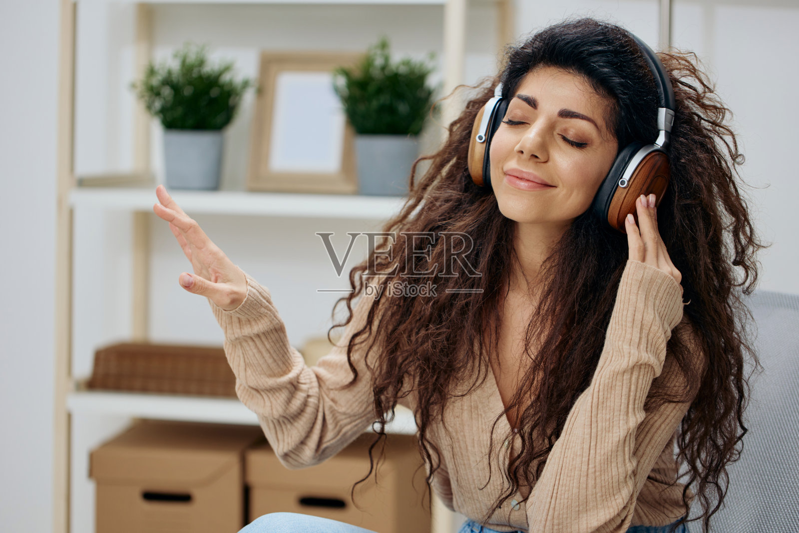 轻松平静愉快的棕褐色卷发拉丁女士带着耳机移动到凉爽的音乐坐在椅子上在家里现代室内闭上眼睛。复制空间模拟横幅。概念冥想。在家放松照片摄影图片