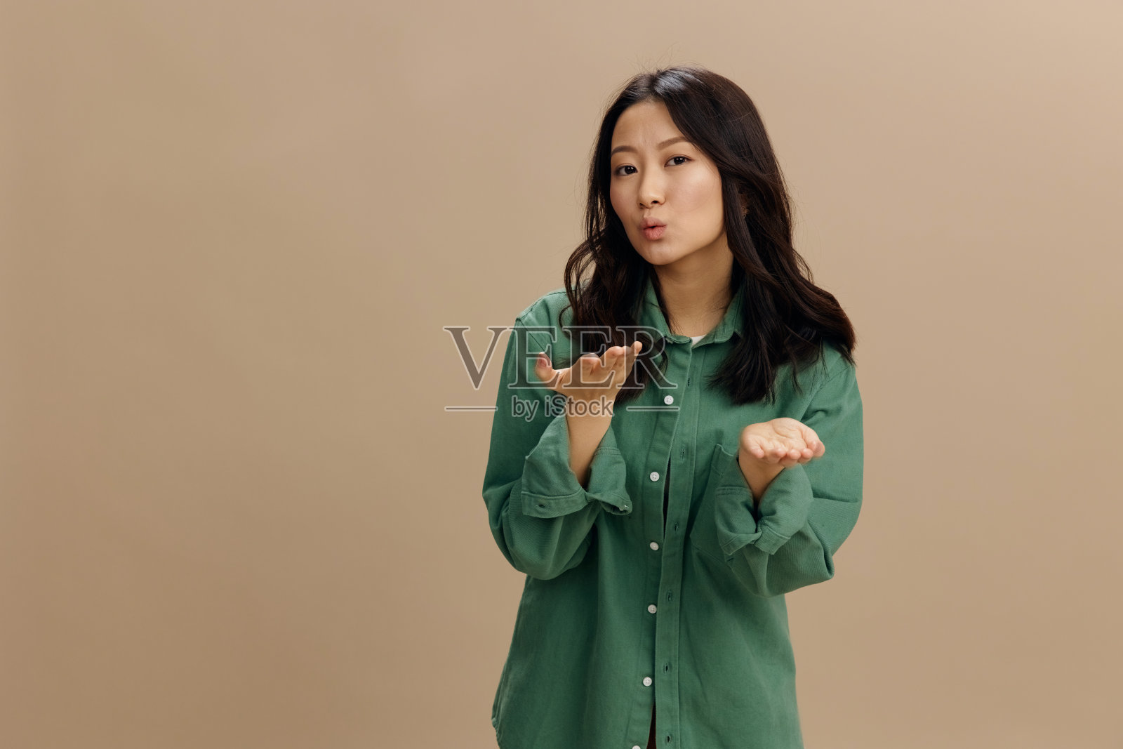 坠入爱河的幸福的亚洲学生年轻女子，穿着卡其绿衬衫，在米色柔和的工作室背景上独自摆姿势，向镜头献吻。很酷的时尚报价。生活方式和情感概念照片摄影图片