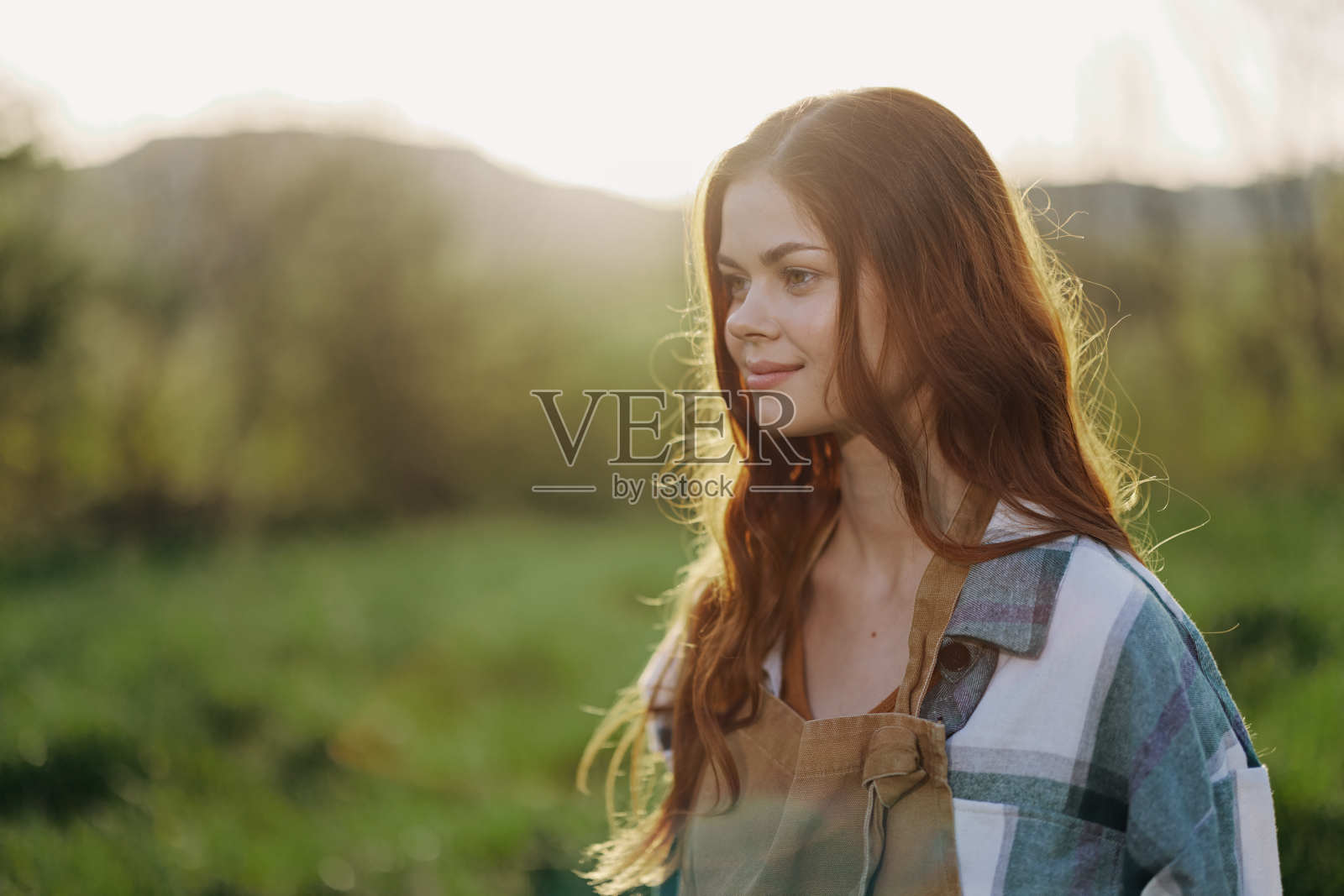 下班后的晚上，一个穿着工作服、格子衬衫、系着围裙、面带微笑的年轻女子在大自然中的肖像照片摄影图片