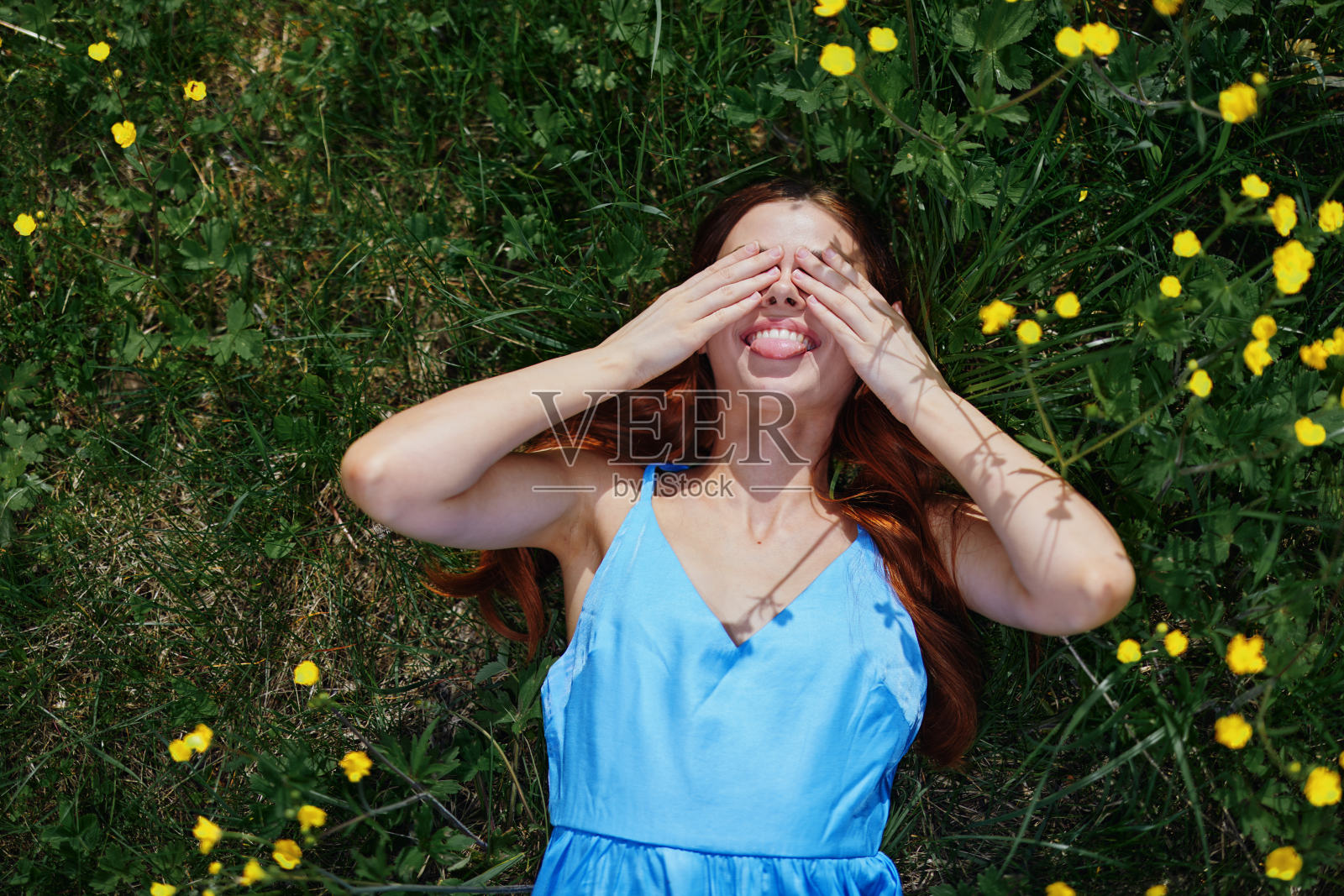 女人笑着闭着眼睛，双手躺在绿草地上开着黄色的花，幸福地长着红色的头发照片摄影图片