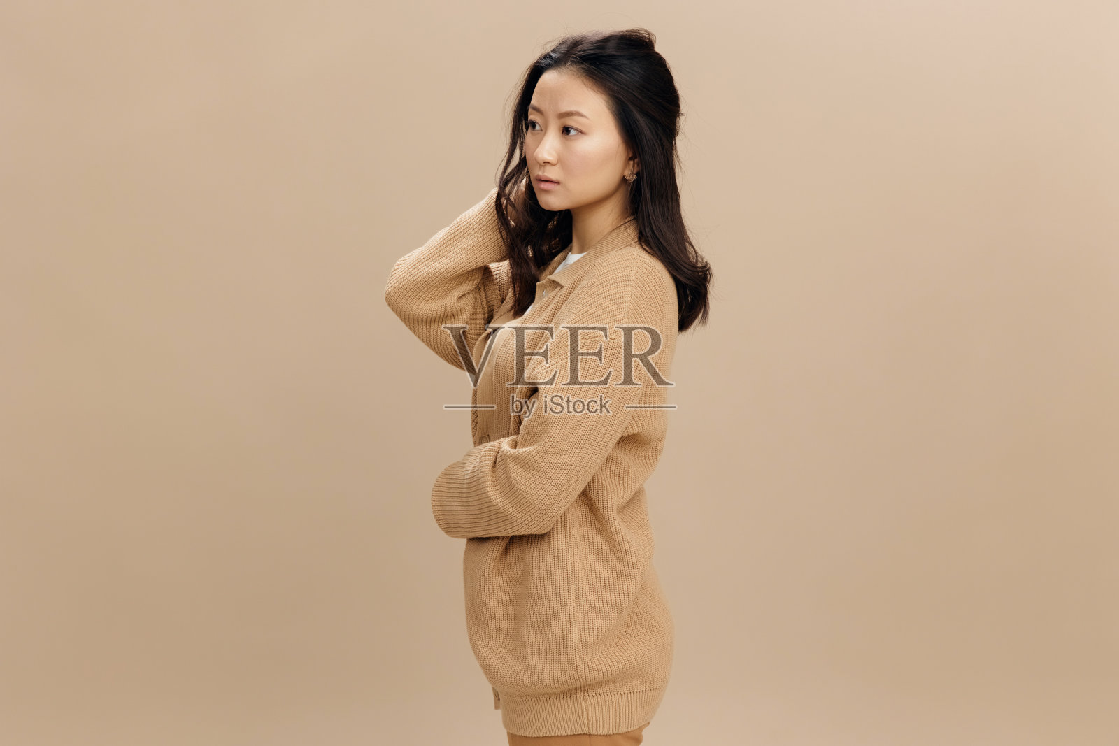 可爱可爱的亚洲学生年轻女子穿着温暖的毛衣，双手叠在米色柔和的工作室背景上，摆出孤立的姿势。很酷的时尚报价。时尚概念照片摄影图片