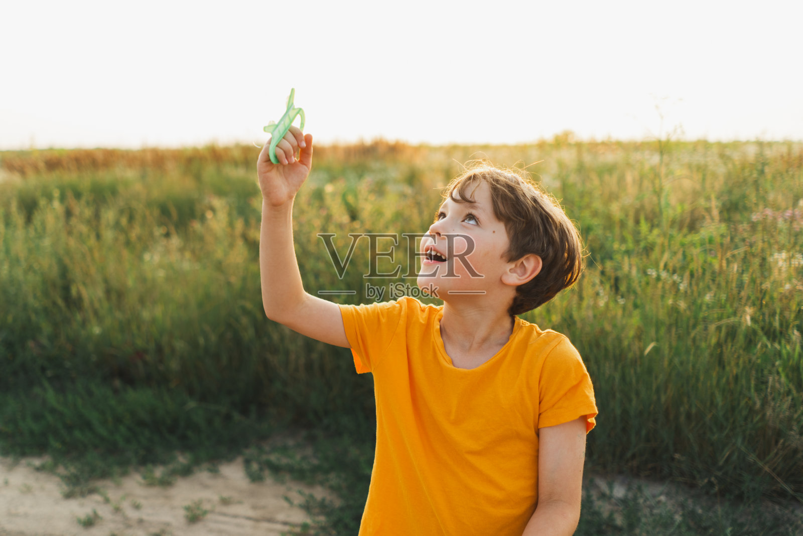 一个穿着橙色t恤的男孩在大自然中放风筝。照片摄影图片