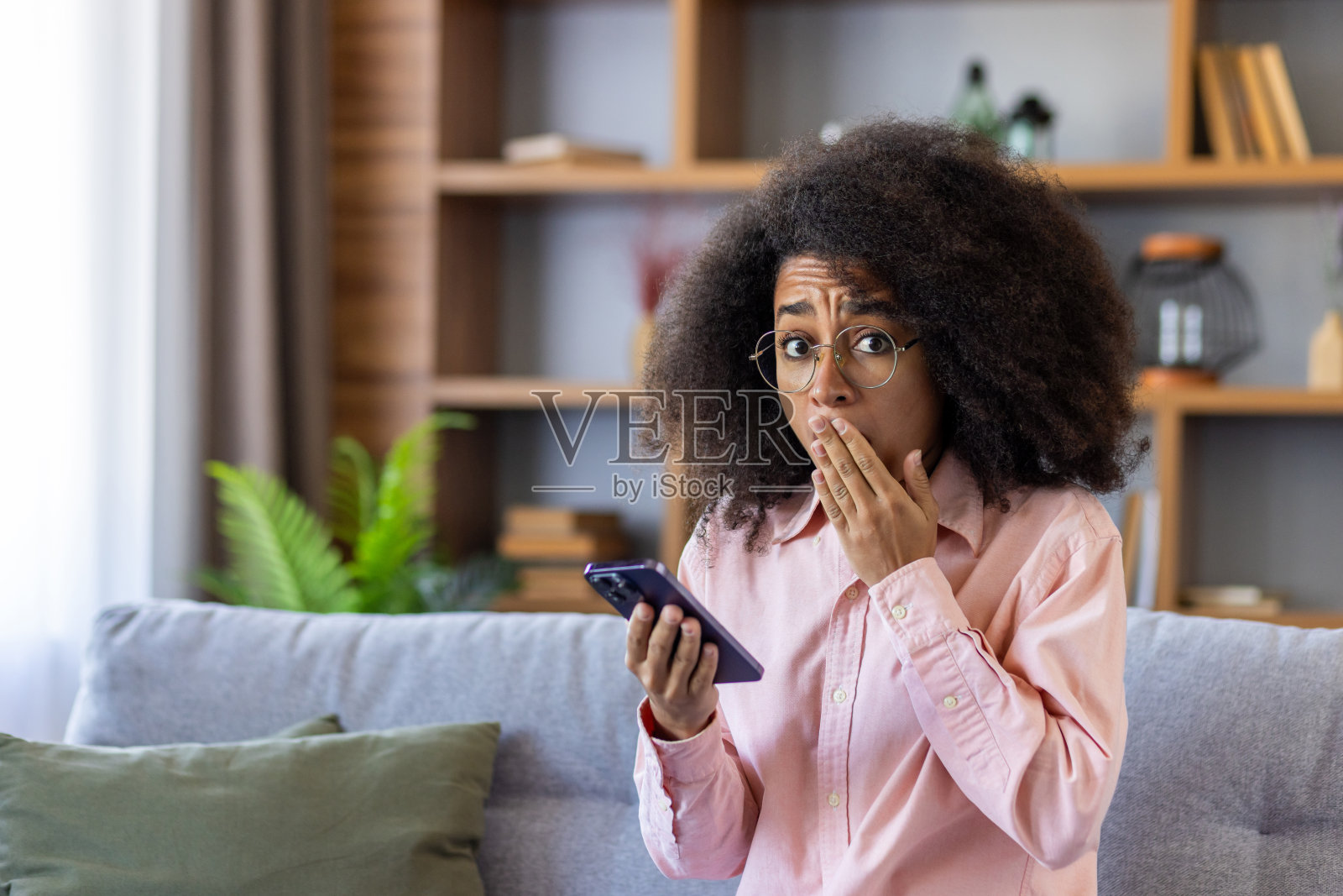 沮丧失望的女子在家里收到了网上发来的消息和坏消息，沮丧的西班牙女子坐在客厅的沙发上看着相机，手里拿着手机照片摄影图片