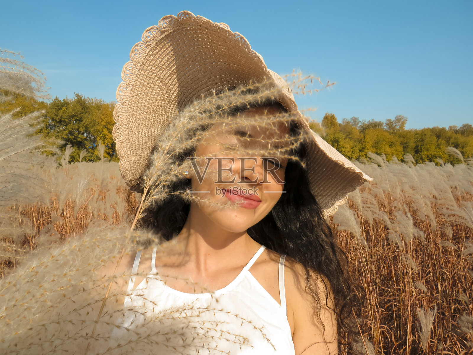 一个戴着帽子的年轻女子站在秋天长满黄草的田野里照片摄影图片