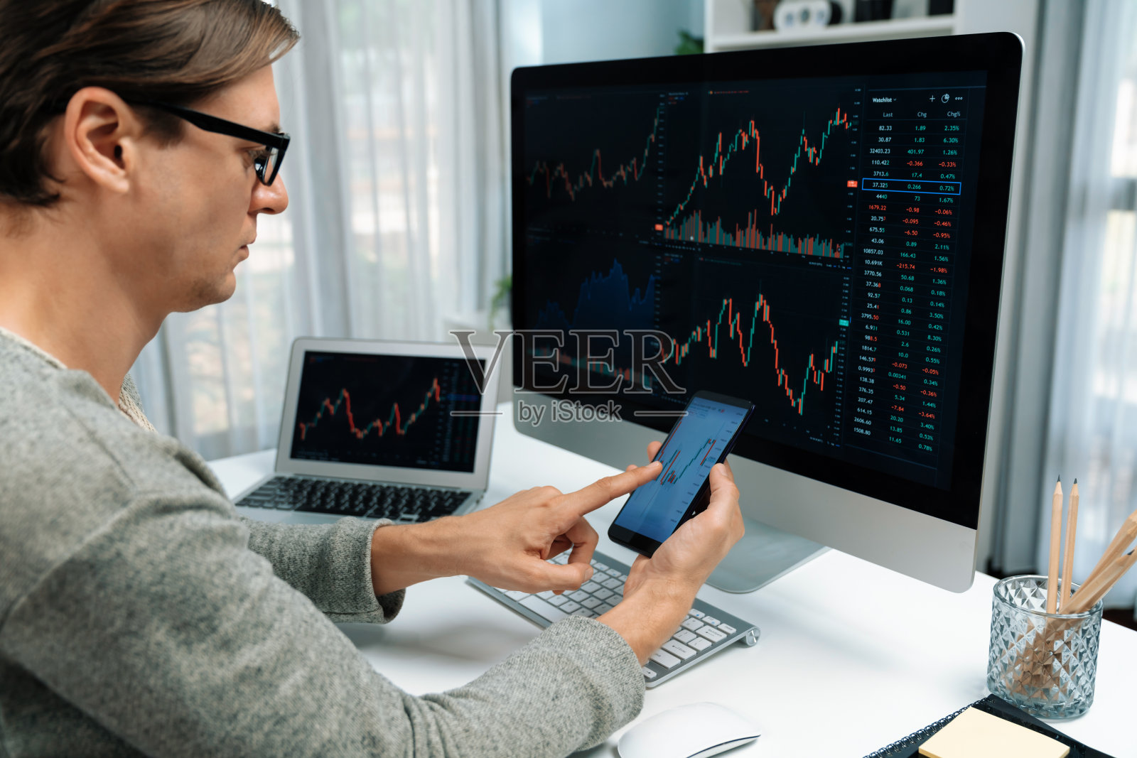 投资者用智能手机指着屏幕，笔记本电脑有库存。金钱。照片摄影图片