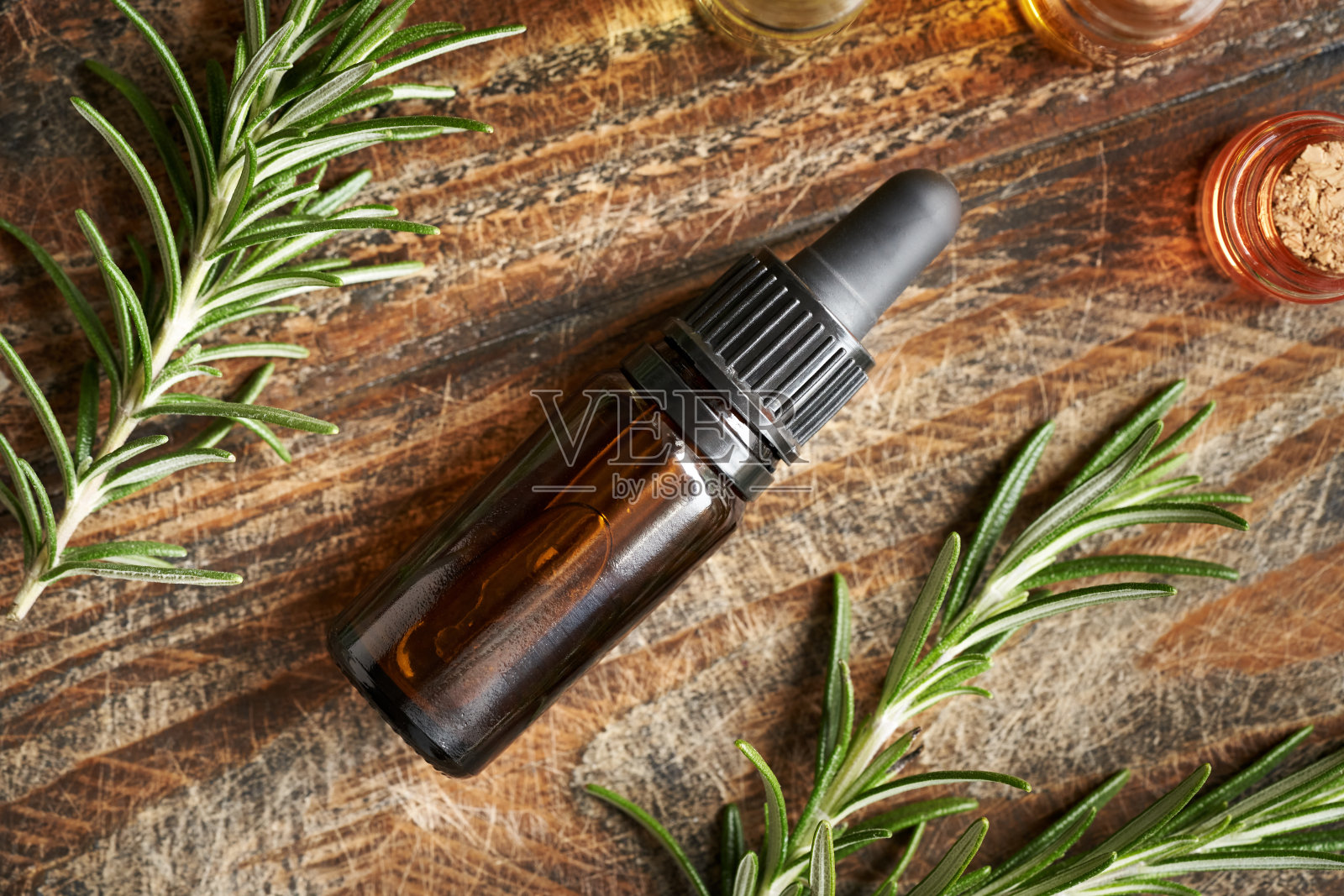 一个棕色的瓶子芳香疗法精油与新鲜盛开的迷迭香植物躺在木制背景照片摄影图片