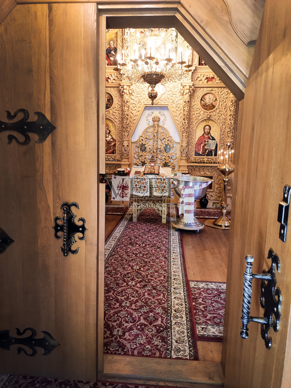 透过一扇敞开的门，可以看到一座基督教东正教教堂，那里有一个洗礼台座和许多耶稣和圣徒的肖像。小而舒适的木制教堂照片摄影图片